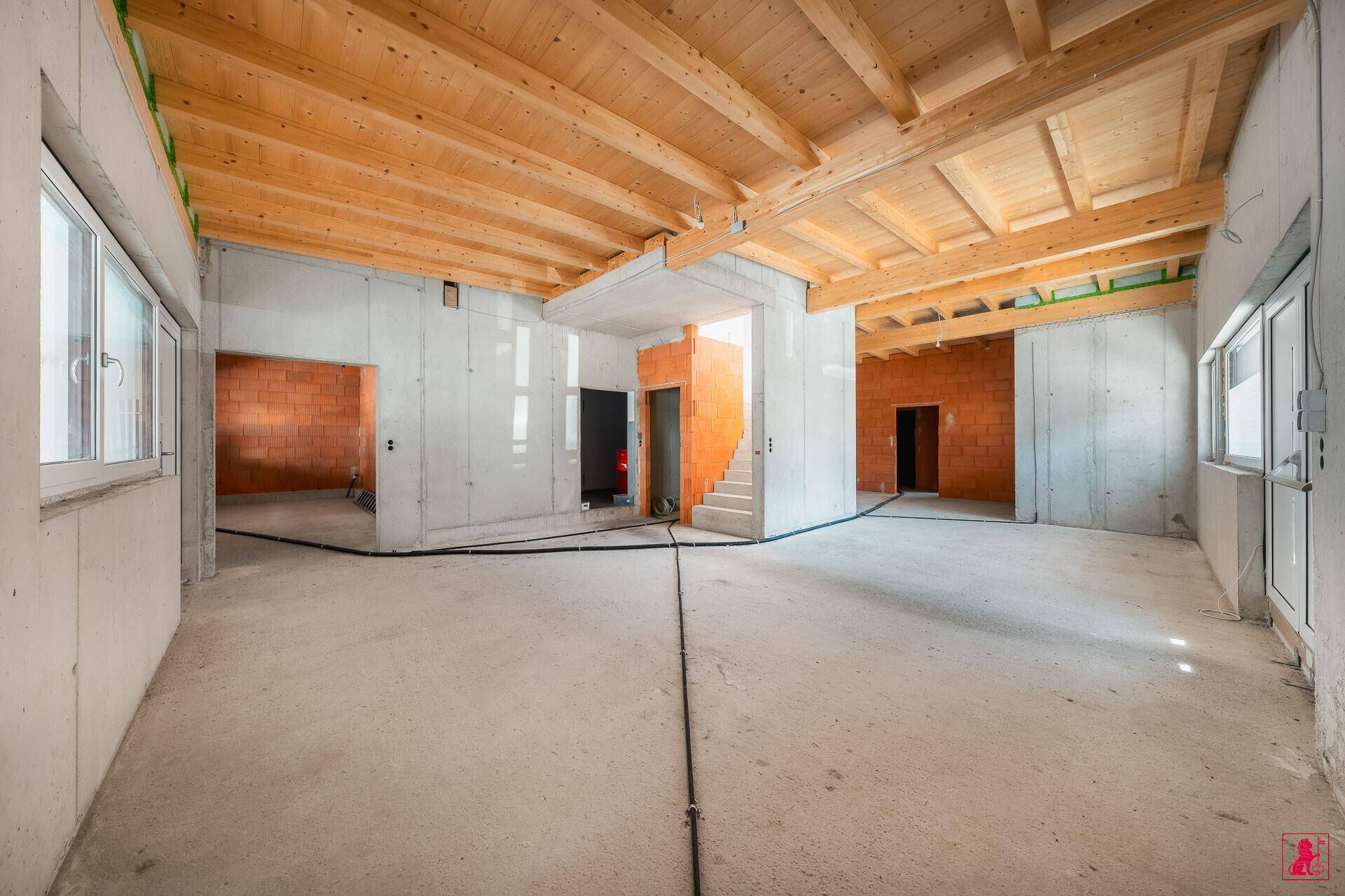 Großer, unfertiger Innenraum mit Sichtbetonwänden, unverputzten Ziegelwänden und Holzbalkendecke.