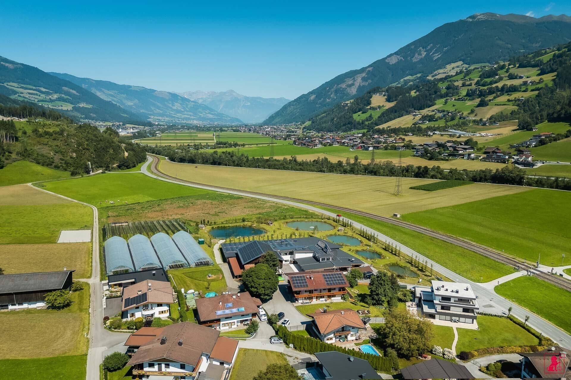 Luftaufnahme der Anlage mit angrenzenden Wohnhäusern und weiten Feldern in einem malerischen Tal.