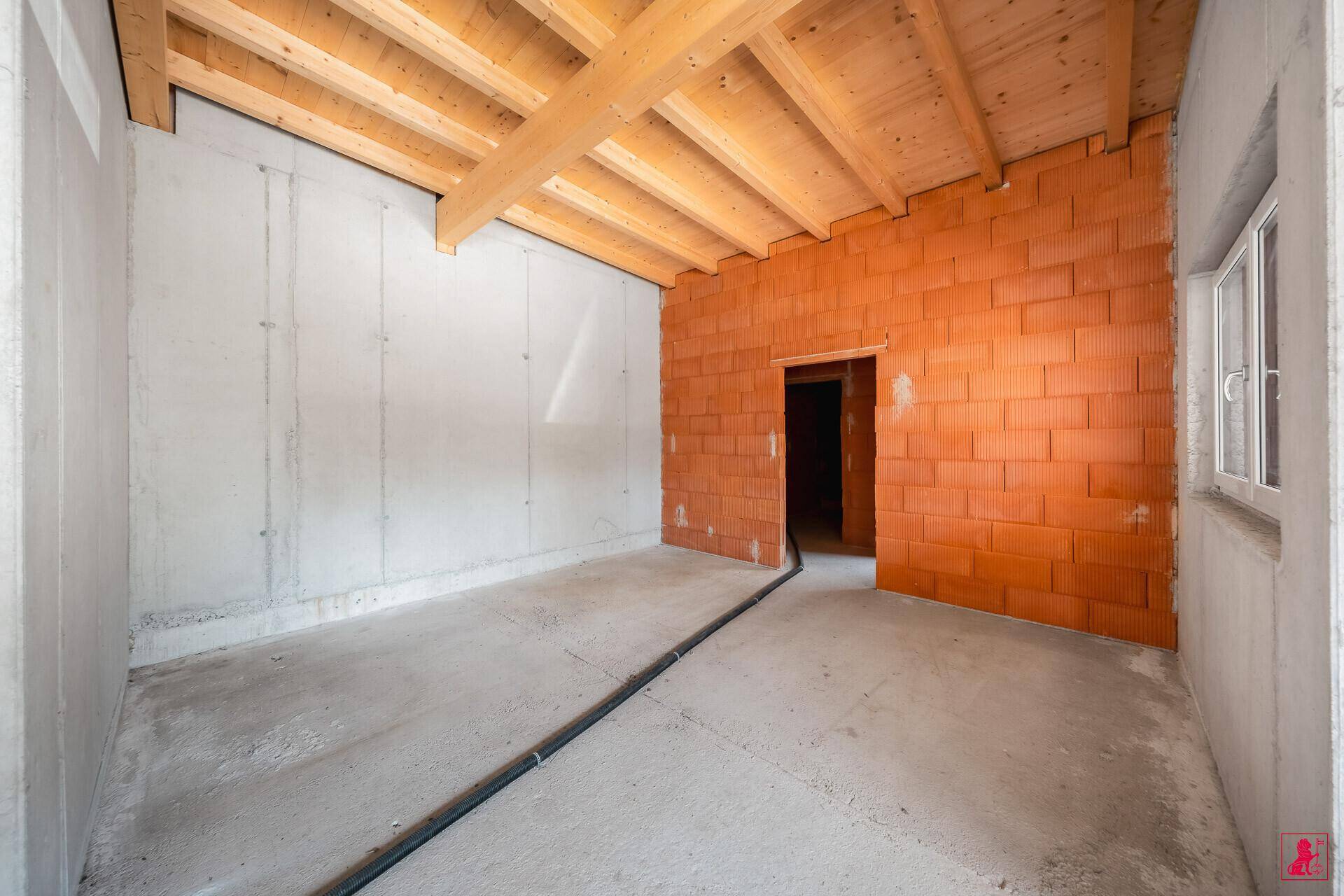 Unfertiger Raum mit einer Kombination aus Sichtbeton- und Ziegelwänden sowie einer Holzbalkendecke.