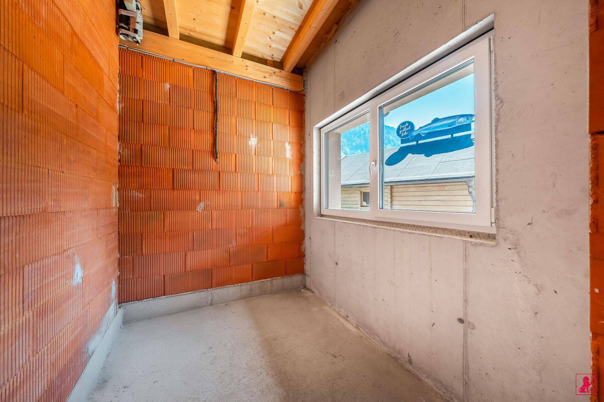 Unfertiger Raum mit Ziegel- und Betonwänden, ausgestattet mit einem Fenster, das Tageslicht hereinlässt.
