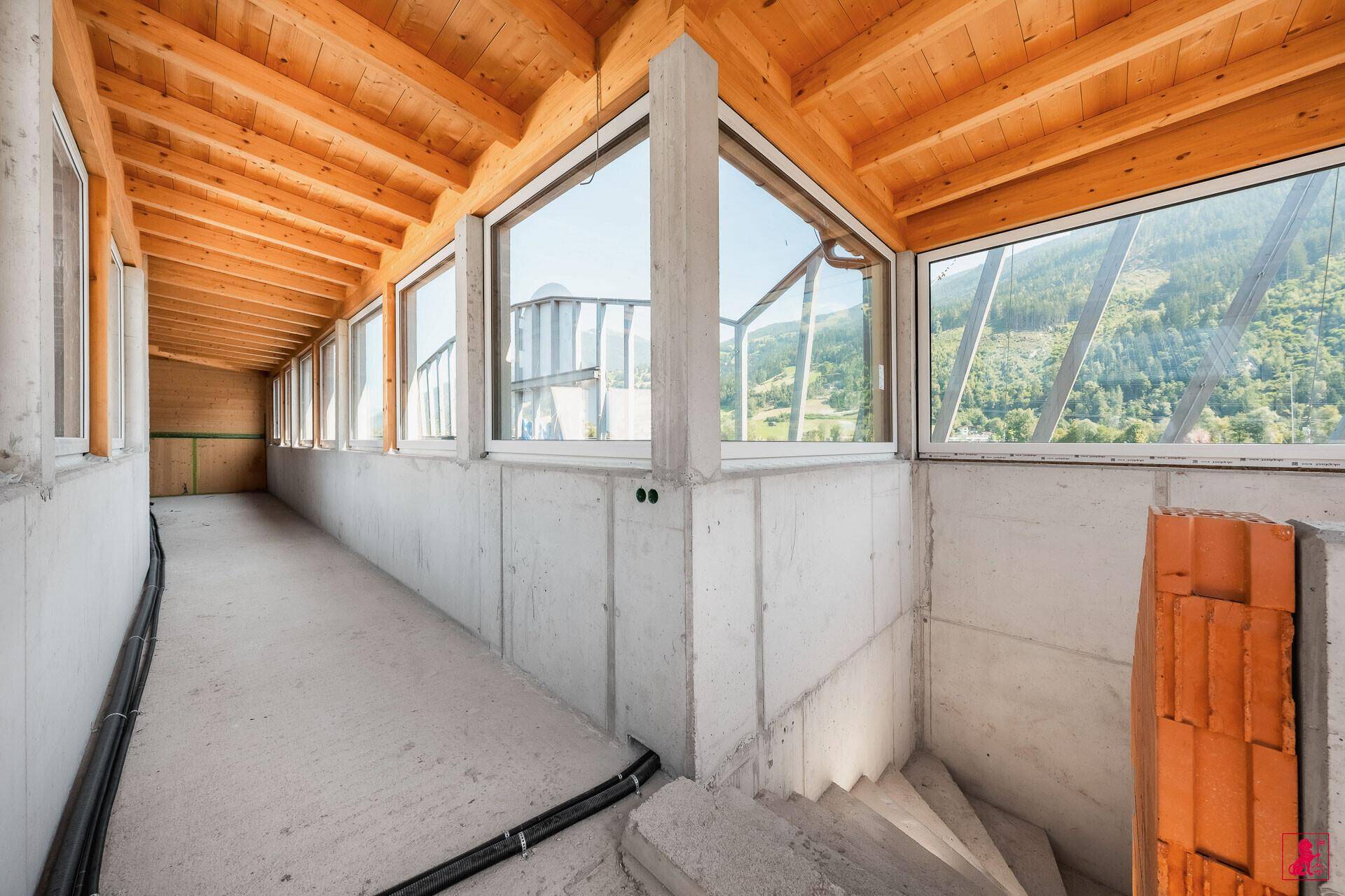 Langer, unfertiger Flur mit großen Fenstern, die einen Panoramablick auf die Landschaft bieten, und einer Holzbalkendecke.