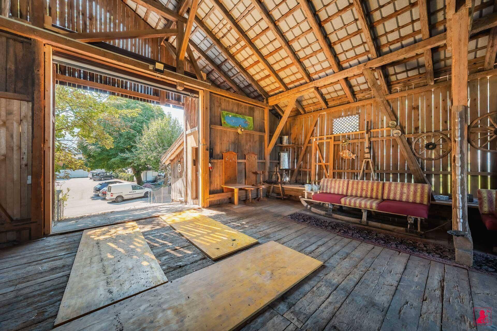 Rustikaler Innenraum einer Scheune mit Holzboden, sichtbaren Balken und traditionellen Möbeln.