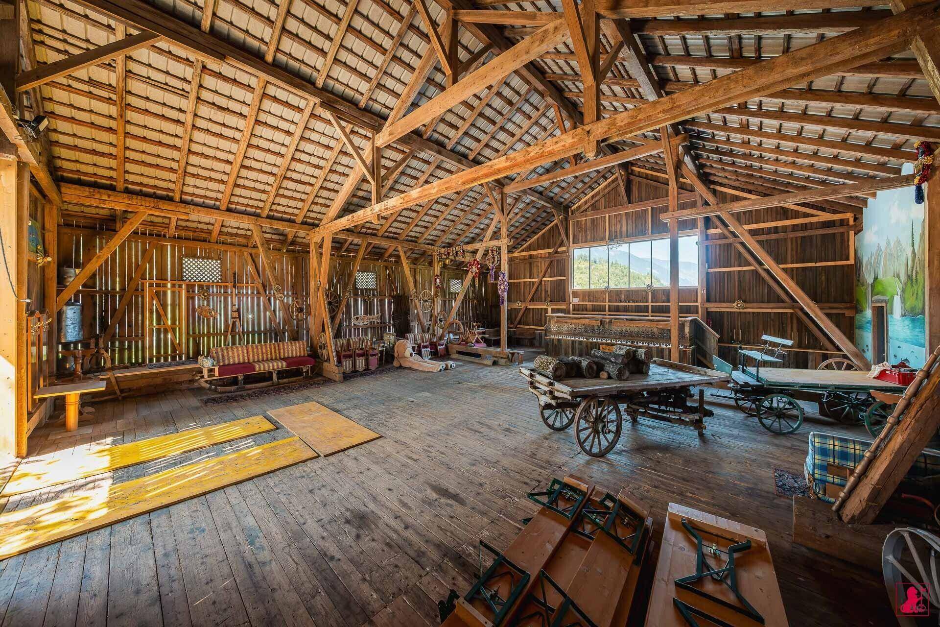 Weitläufiger Scheuneninnenraum mit Holzboden, sichtbaren Dachbalken und historischen landwirtschaftlichen Geräten.
