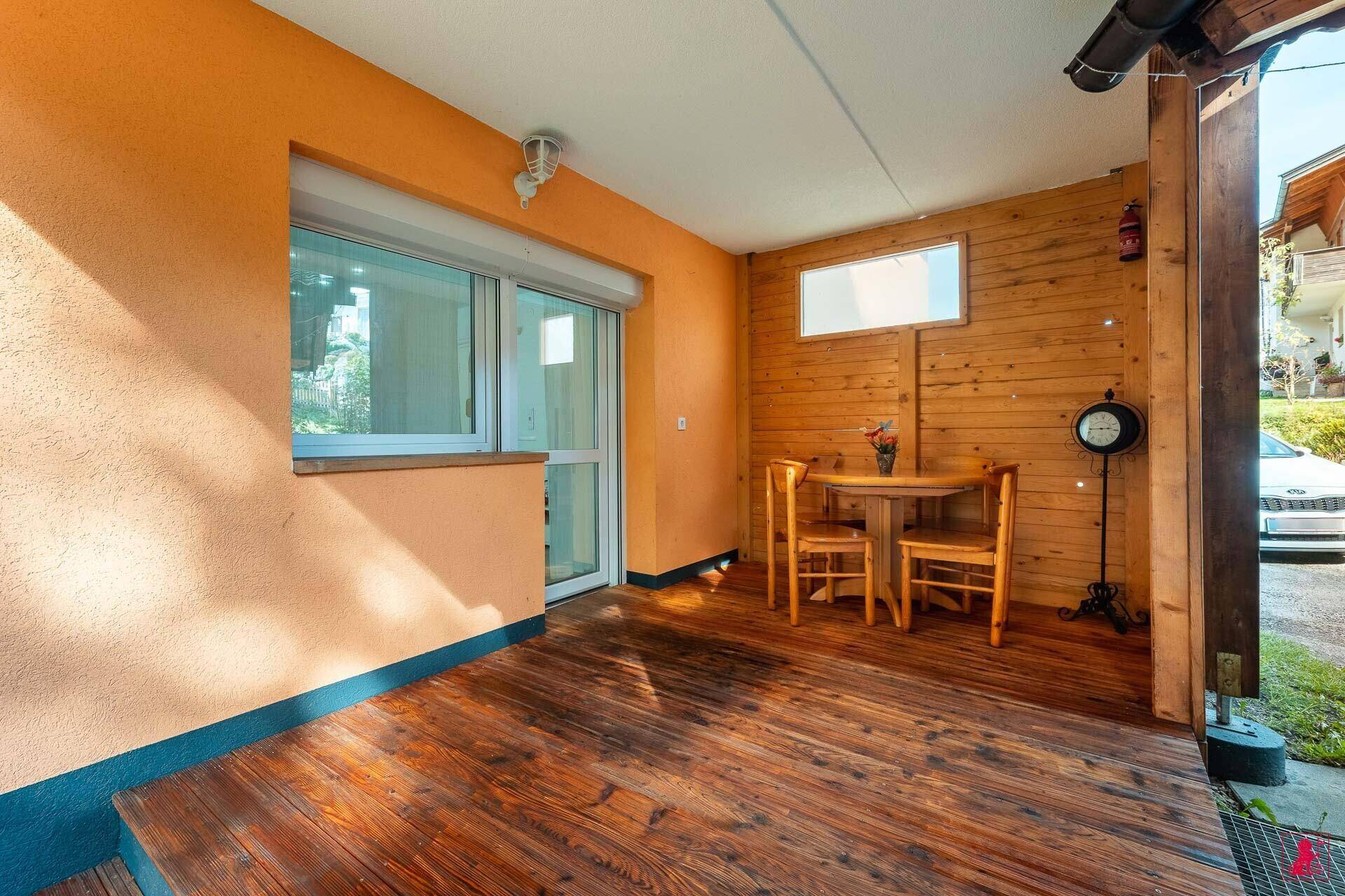 Gemütliche, überdachte Holzterrasse mit Esstisch und Stühlen, ideal für Mahlzeiten im Freien.