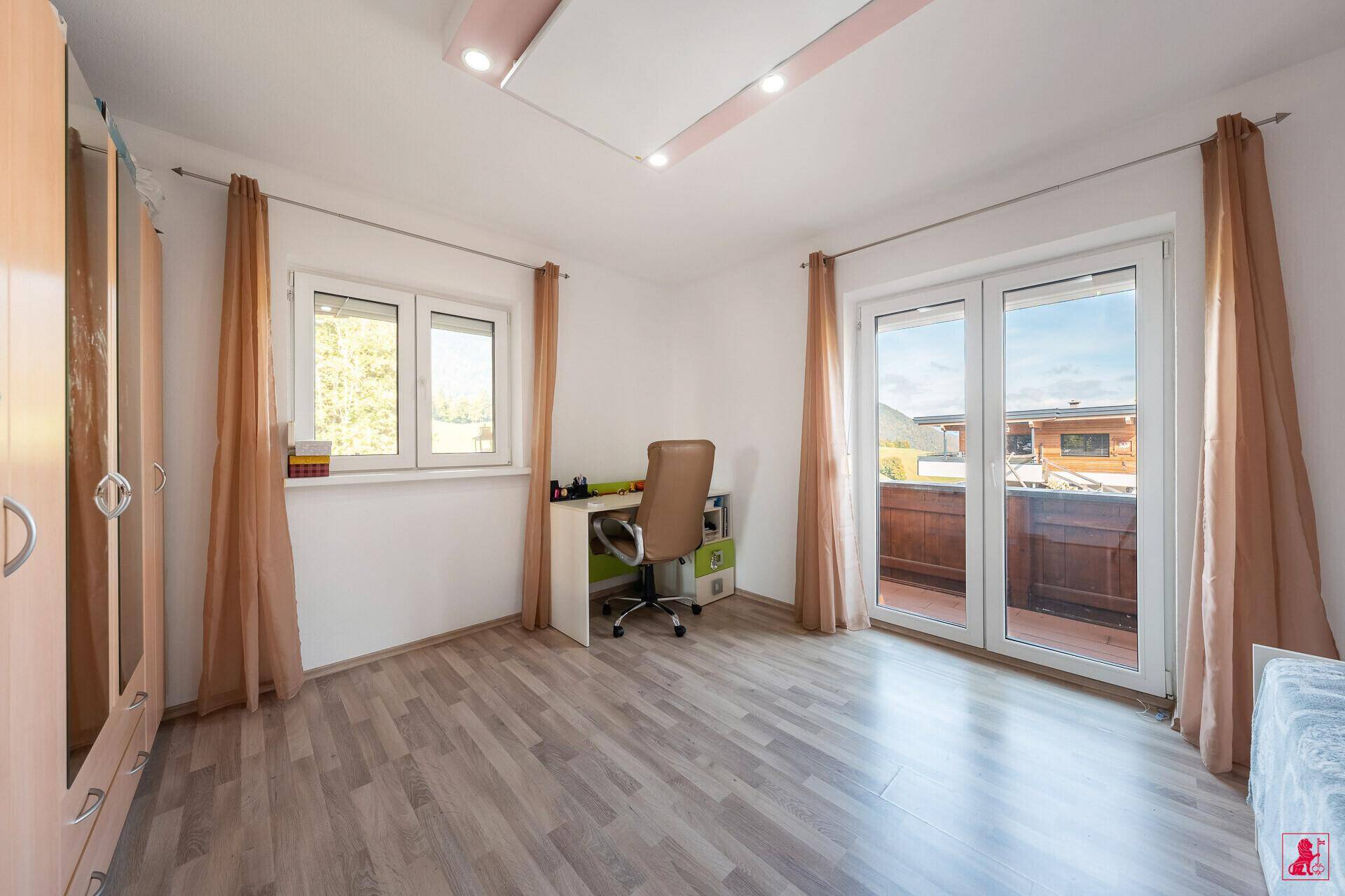 Helles Schlafzimmer mit Schreibtisch, Holzboden und Zugang zum Balkon.