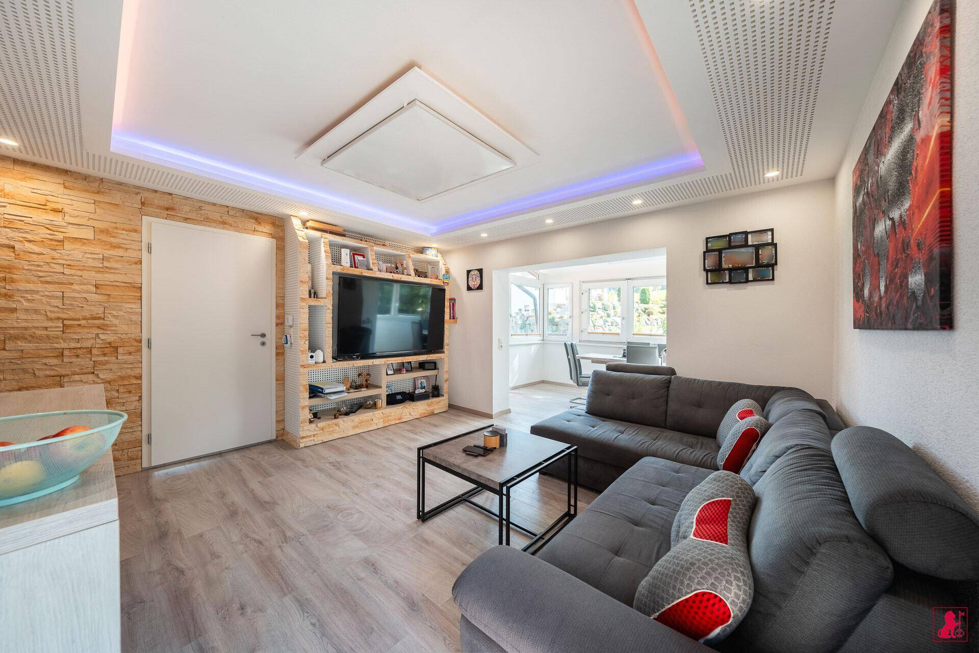 Gemütliches Wohnzimmer mit großem Sofa, Fernseher und indirekter Deckenbeleuchtung.
