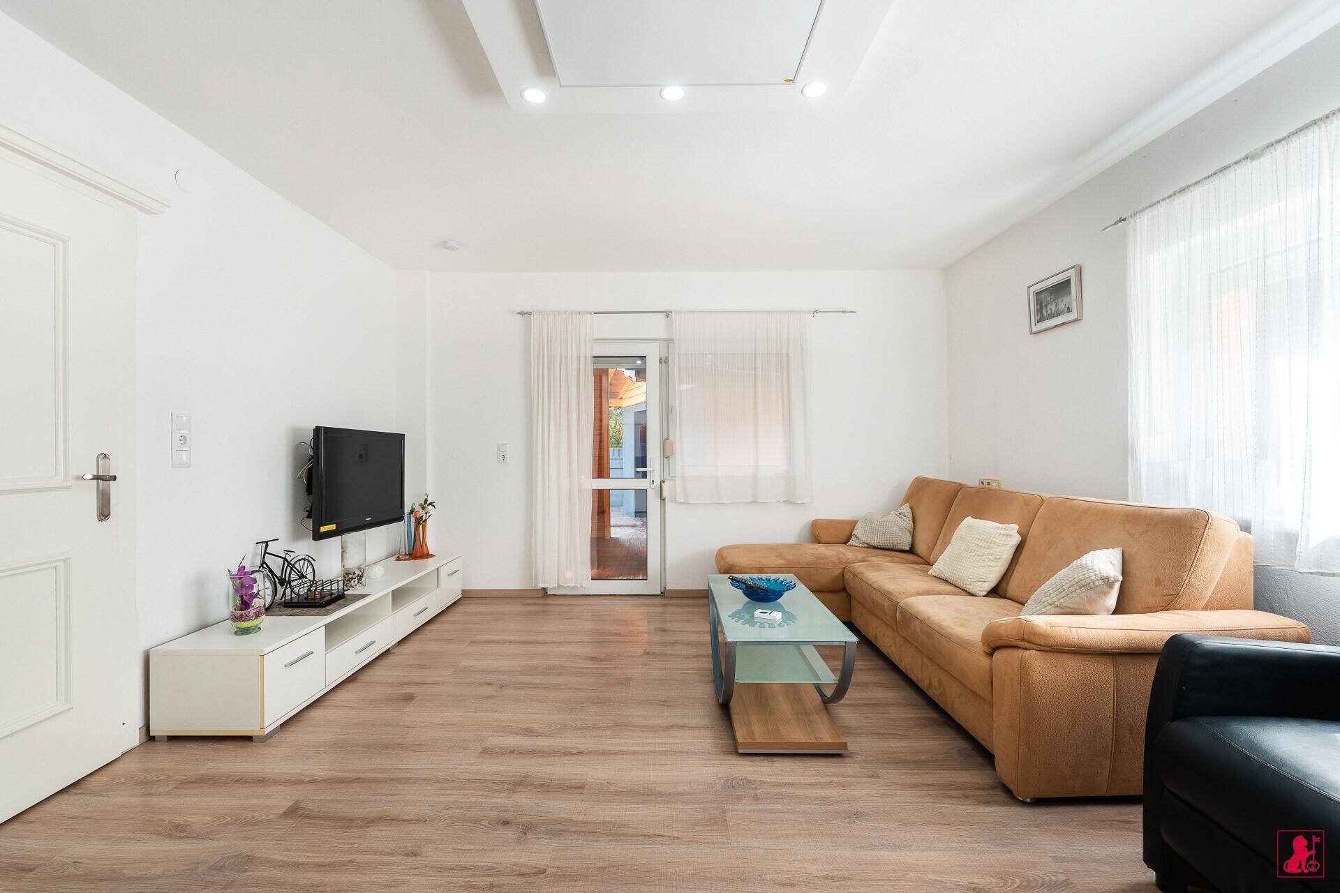 Gemütliches Wohnzimmer mit großem Ecksofa, Fernseher und Zugang zum Außenbereich.