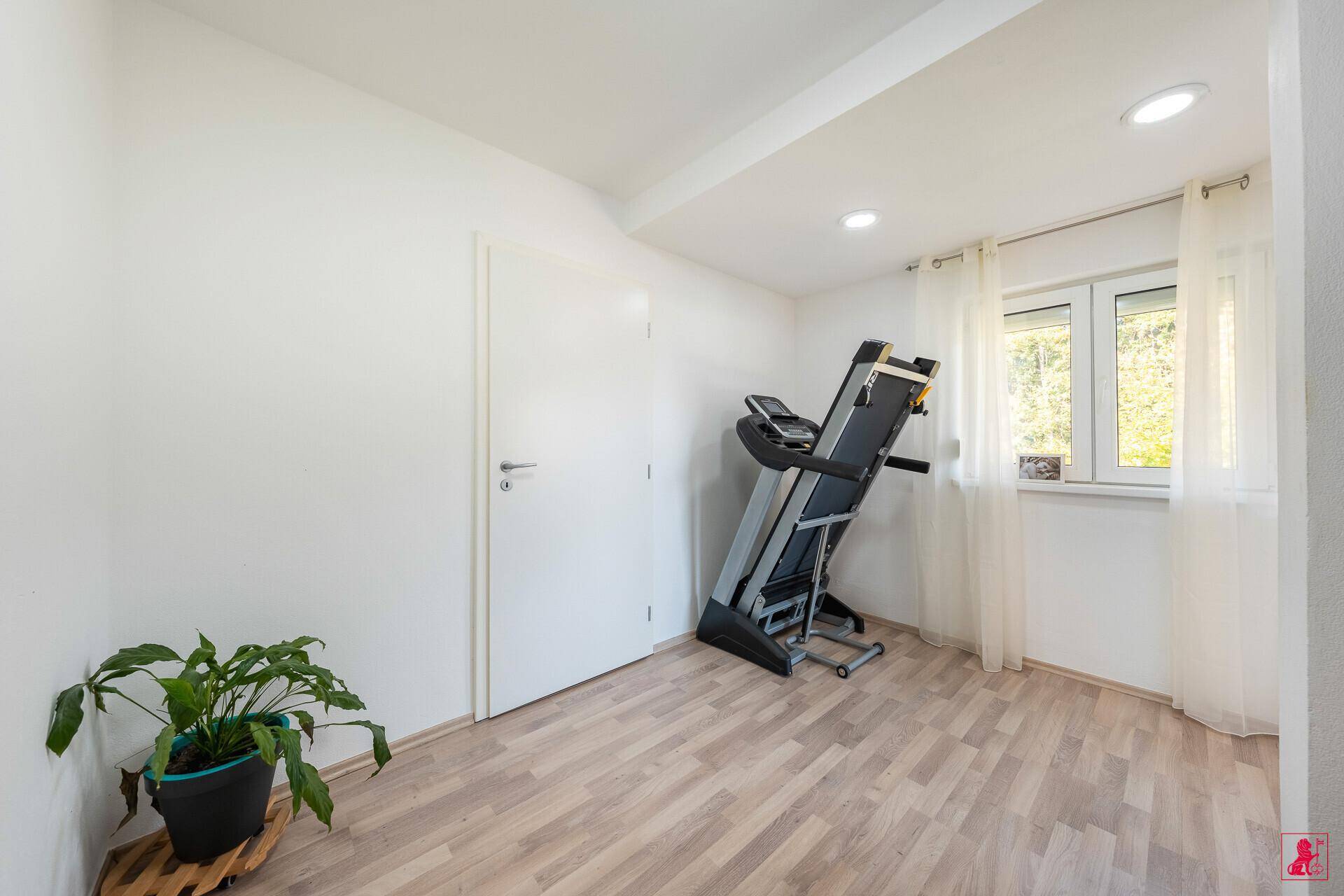 Heller Raum mit Laufband, Holzboden und Fenster mit Blick ins Grüne.
