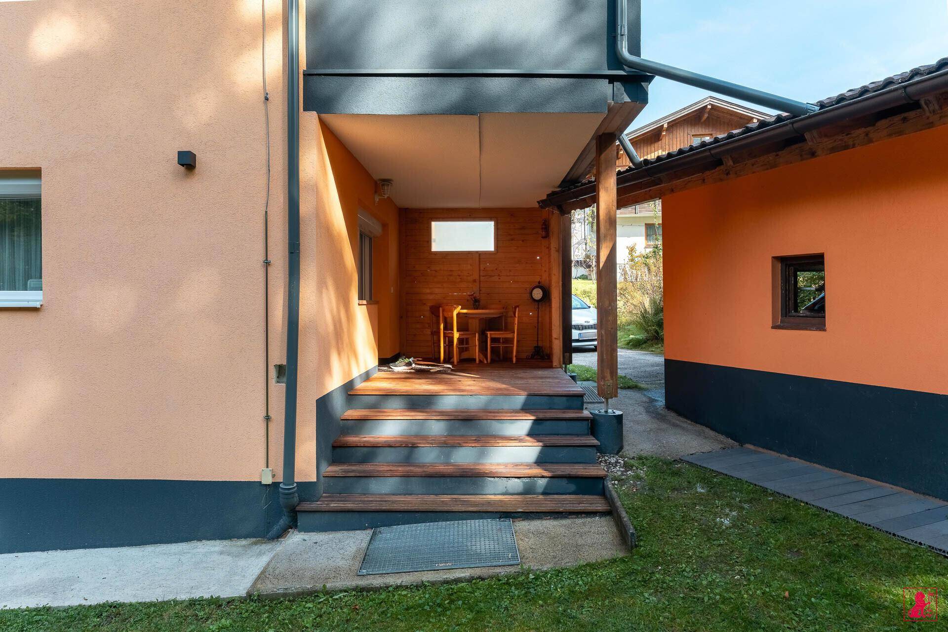 Überdachte Holzterrasse mit rustikalen Holzstufen und Zugang zum Gartenbereich des Hauses.