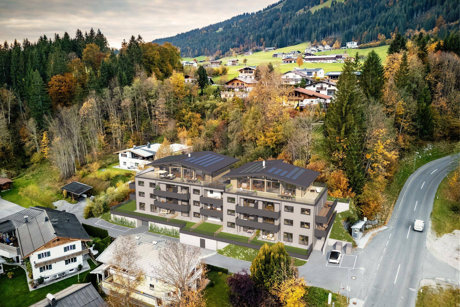 Moderne Wohnanlage in alpiner Umgebung, eingebettet in grüne Hügel mit Herbstbäumen.