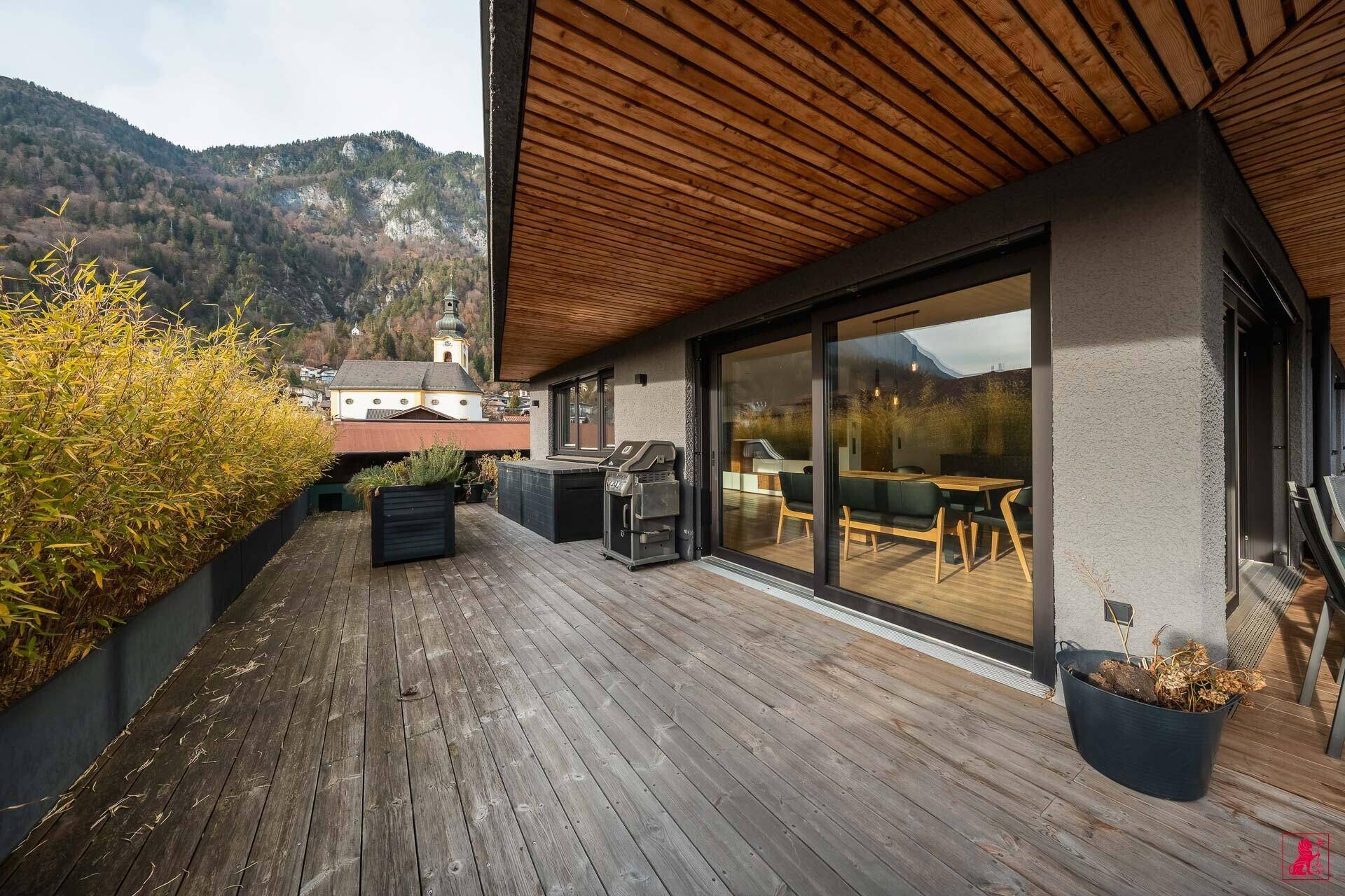 Holzterrasse mit Grillbereich und Blick auf die umliegende Berglandschaft und Kirche.
