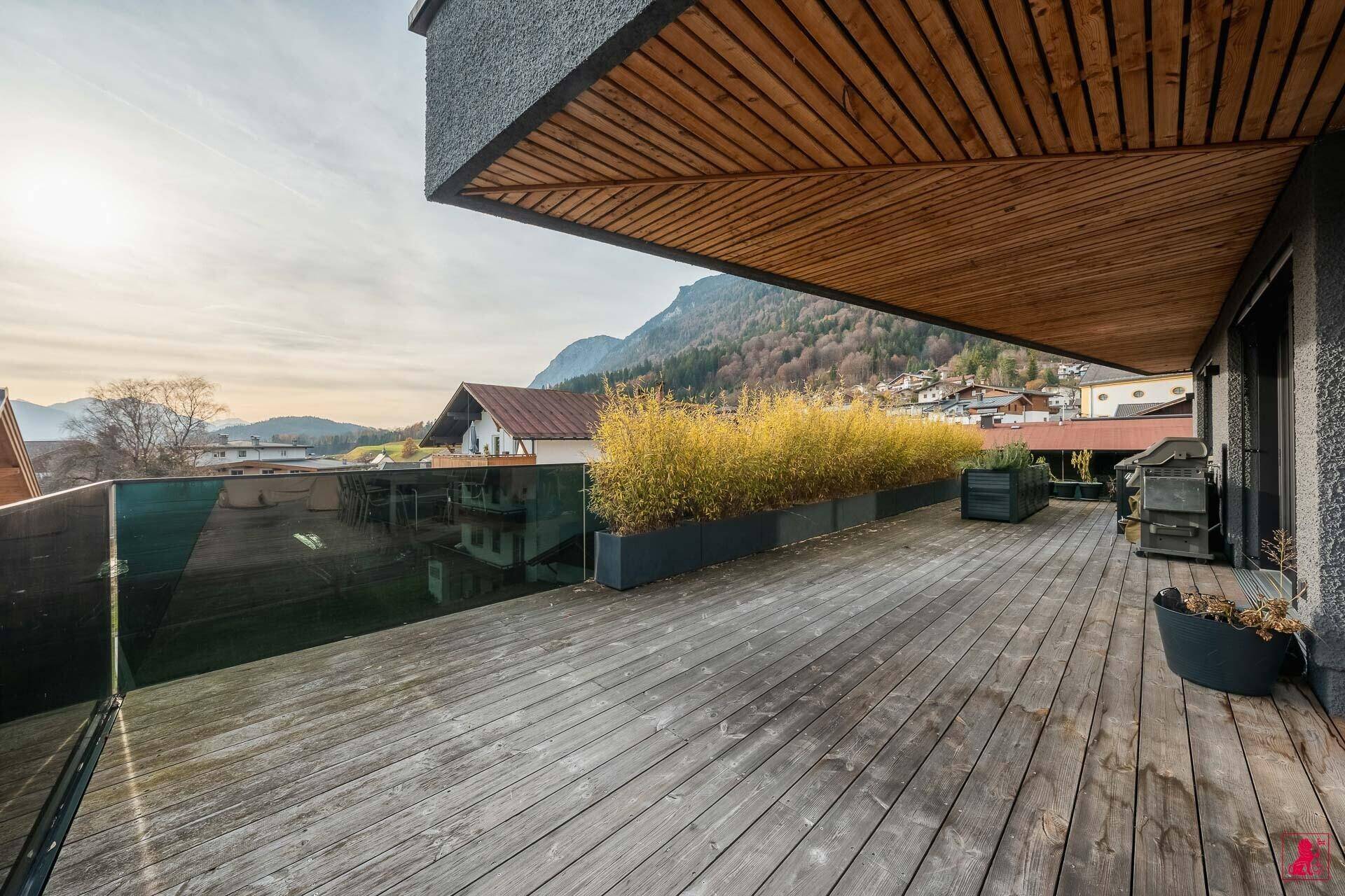 Große Holzterrasse mit Pflanzenkübeln und Blick auf die Berge und das Tal.
