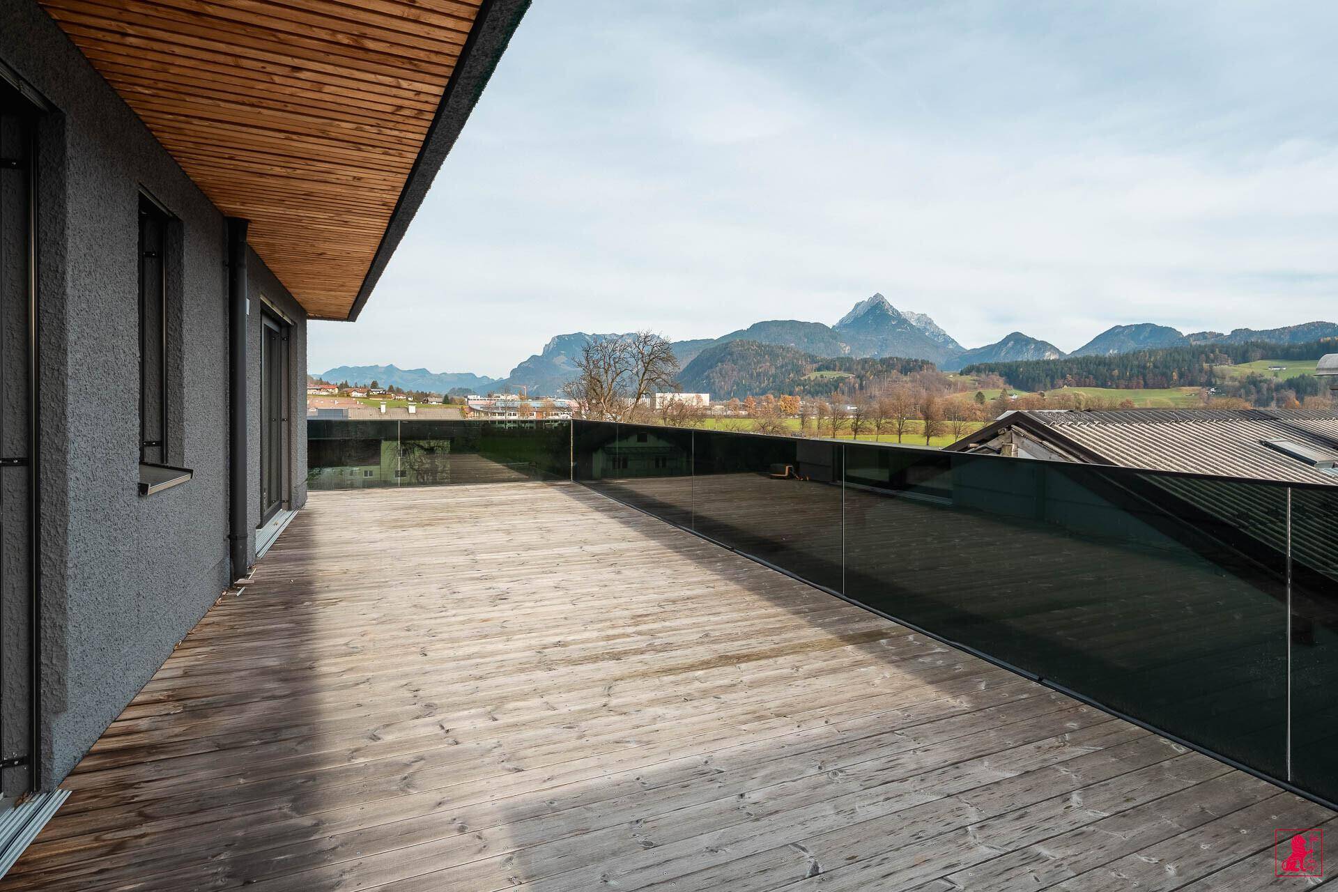 Weitläufige Holzterrasse mit Glasgeländer und Panoramablick auf die umliegende Berglandschaft.