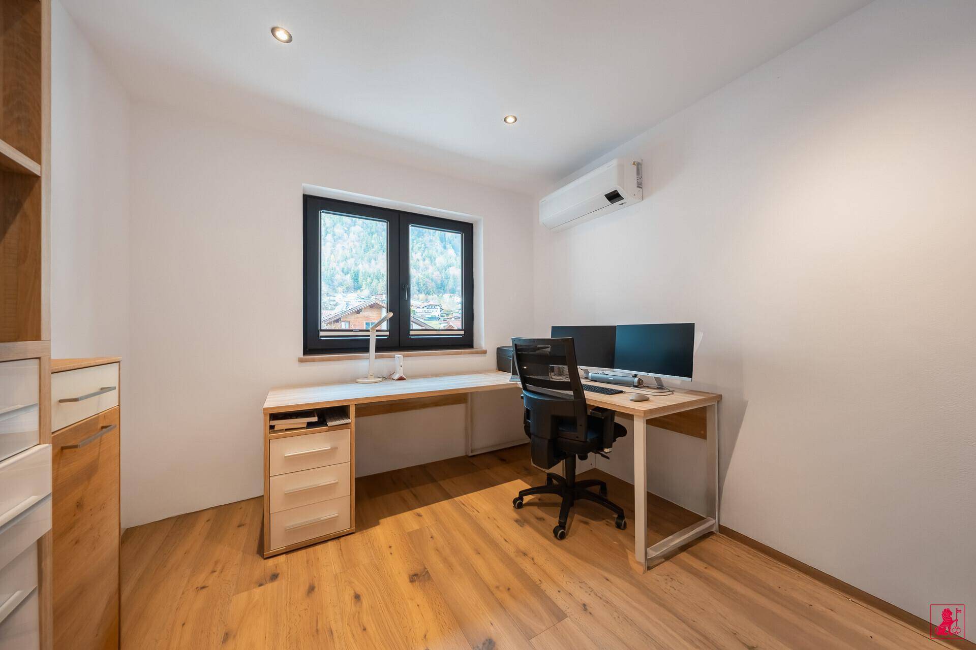 Funktionales Büro mit Schreibtisch, Bürostuhl und Blick ins Grüne durch das Fenster.