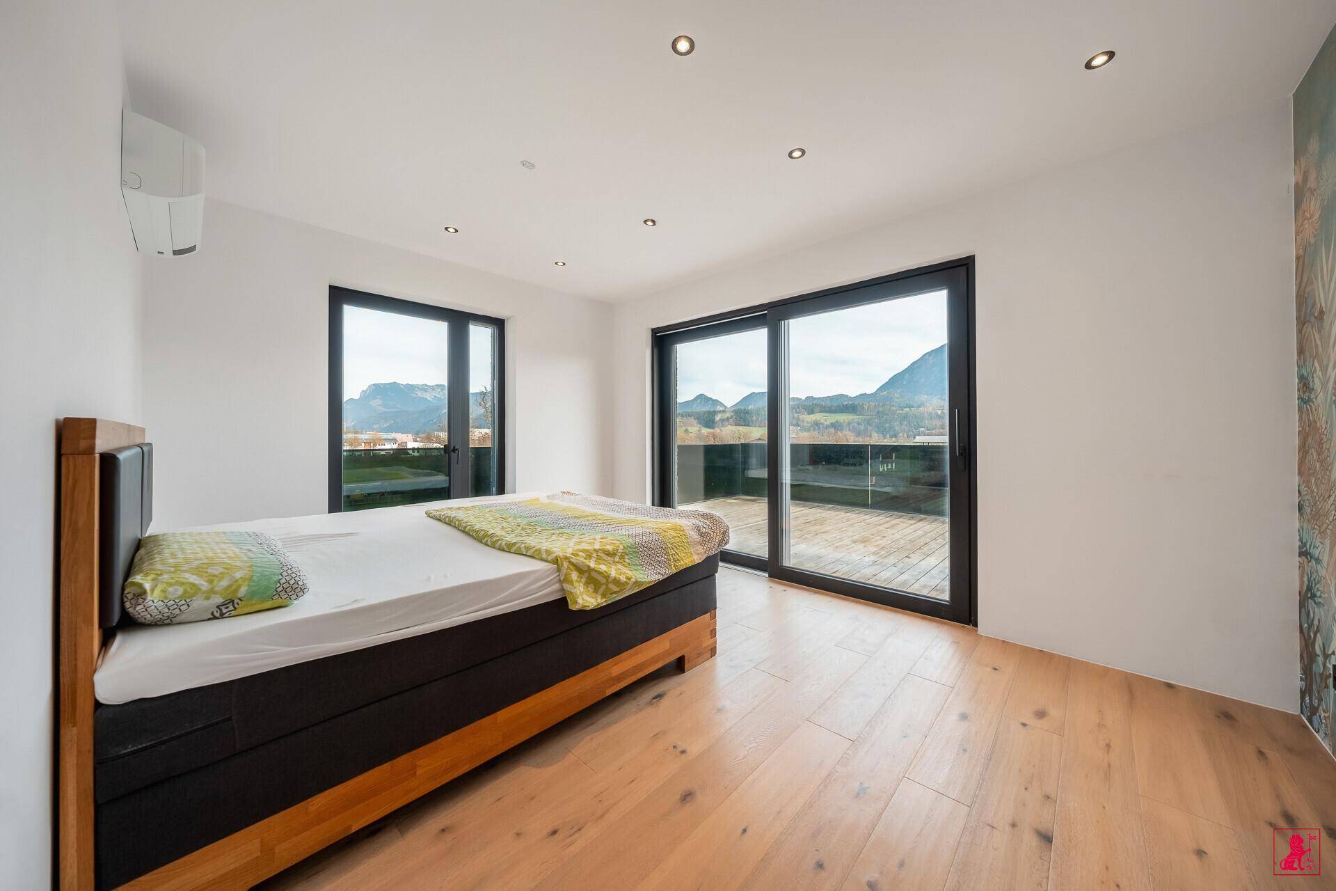 Helles Schlafzimmer mit Holzbett, Parkettboden und Zugang zur Terrasse mit Bergblick.