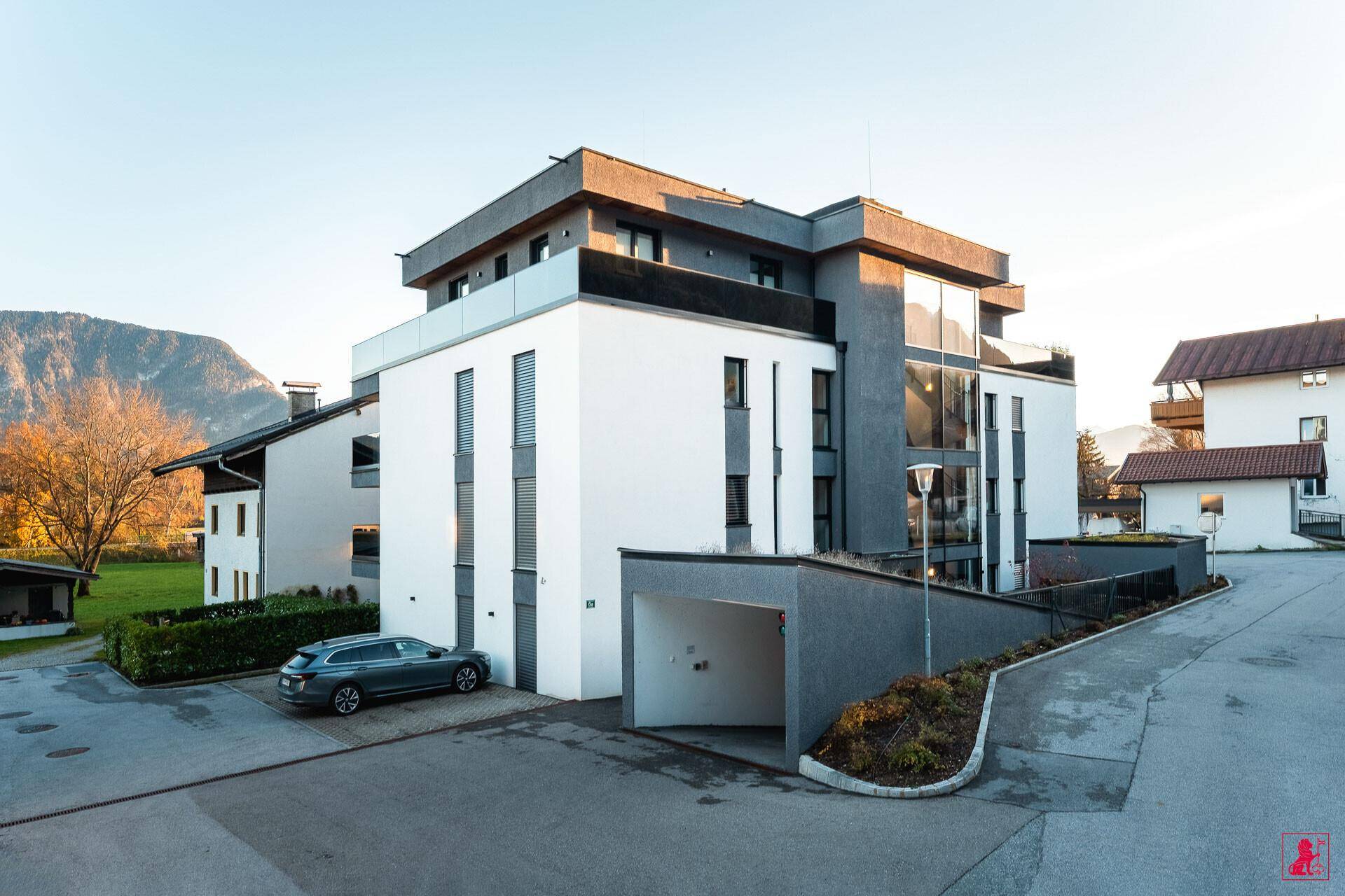 Modernes Wohngebäude mit weißer und grauer Fassade, großen Fenstern und Tiefgaragenzufahrt.