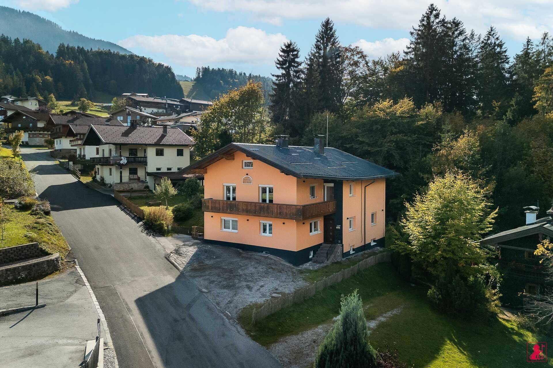 Ansicht des orangefarbenen Hauses mit Holzbalkonen und grüner Umgebung.