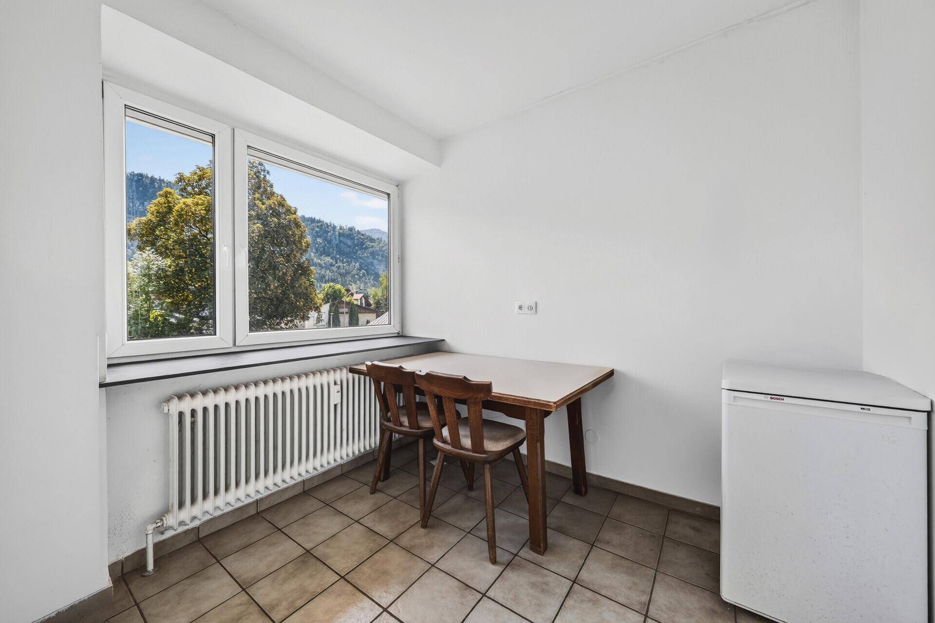 Essbereich in der Küche mit kleinem Tisch, zwei Stühlen und Bergblick durch das Fenster.