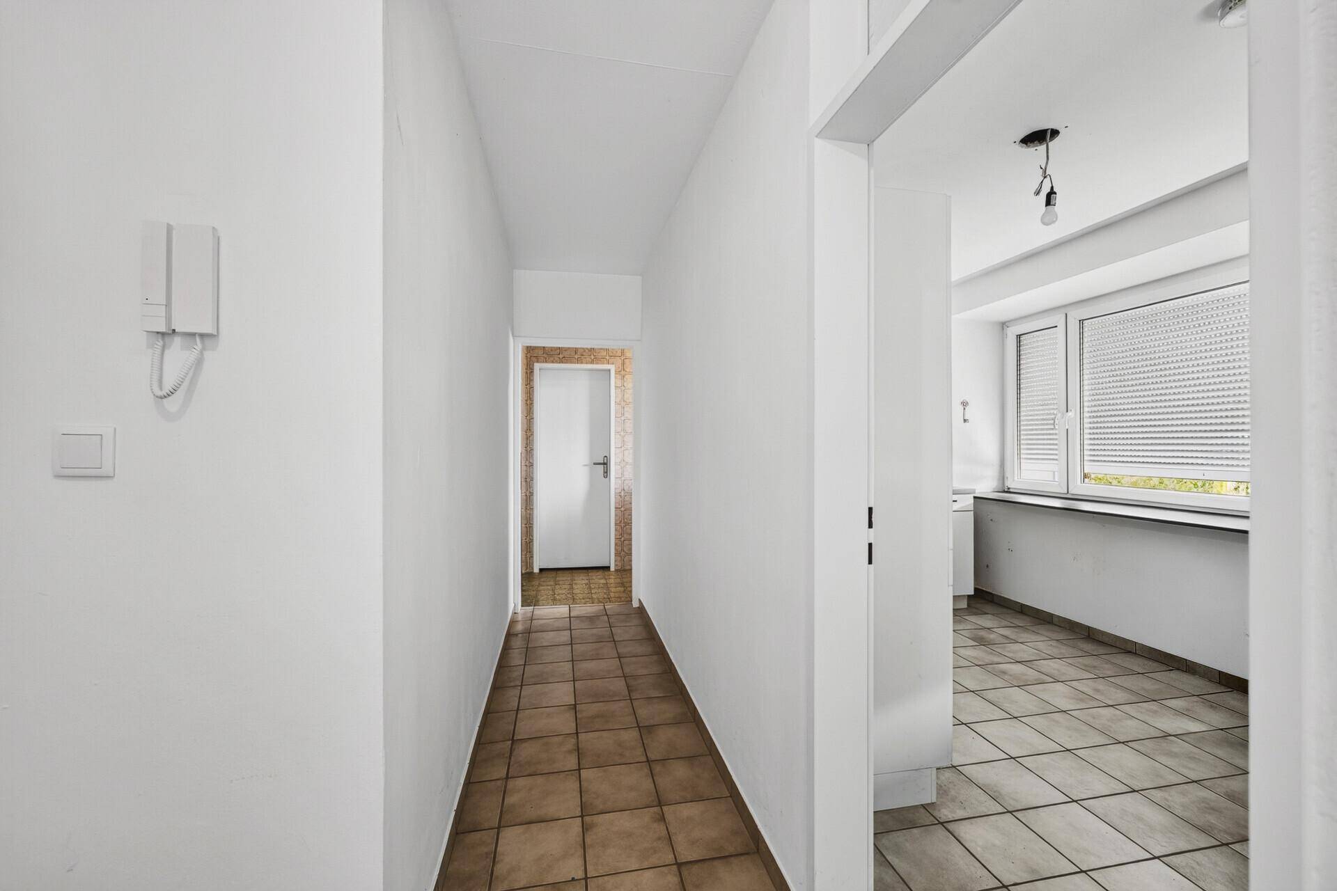 Langer Flur mit Fliesenboden und Zugang zu verschiedenen Zimmern der Wohnung.