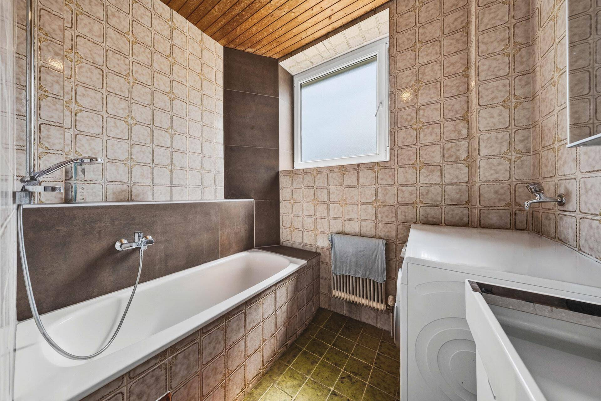 Badezimmer mit Badewanne, Fliesen an Wänden und Boden sowie einer Holzdecke.