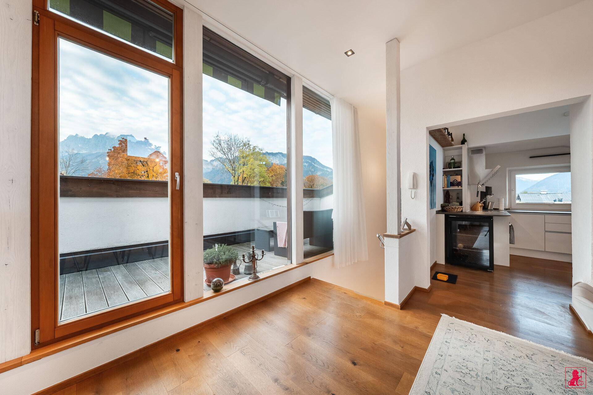 Heller Wohnbereich mit Holzboden, großen Fenstern und Zugang zu einem Balkon mit Bergblick.