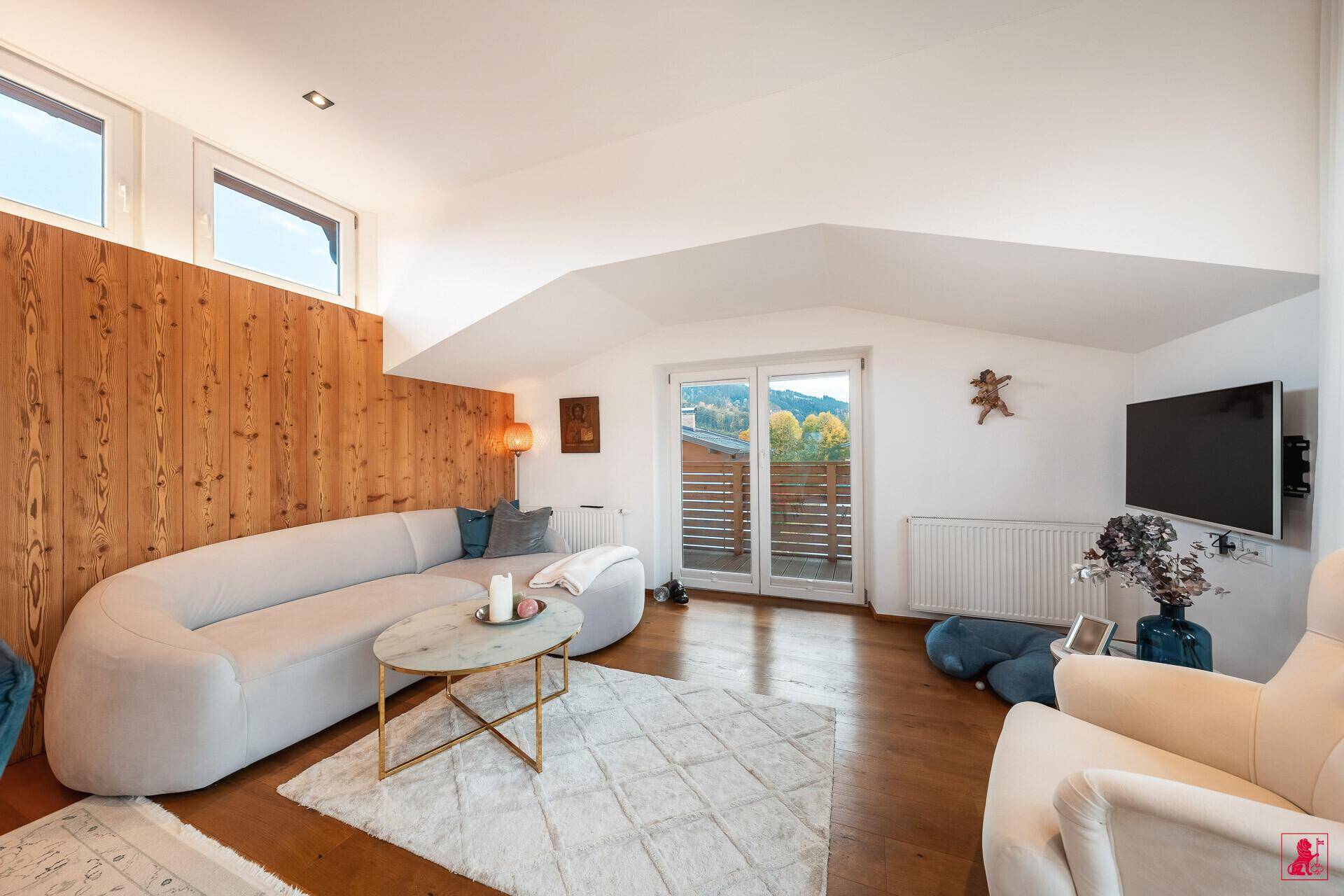Gemütliches Wohnzimmer mit Holzwand, bequemer Couch und Zugang zum Balkon.