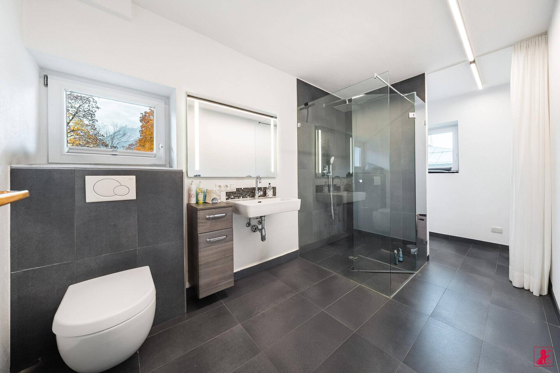 Modernes Badezimmer mit dunklen Fliesen, wandhängendem WC und großer Glasdusche.