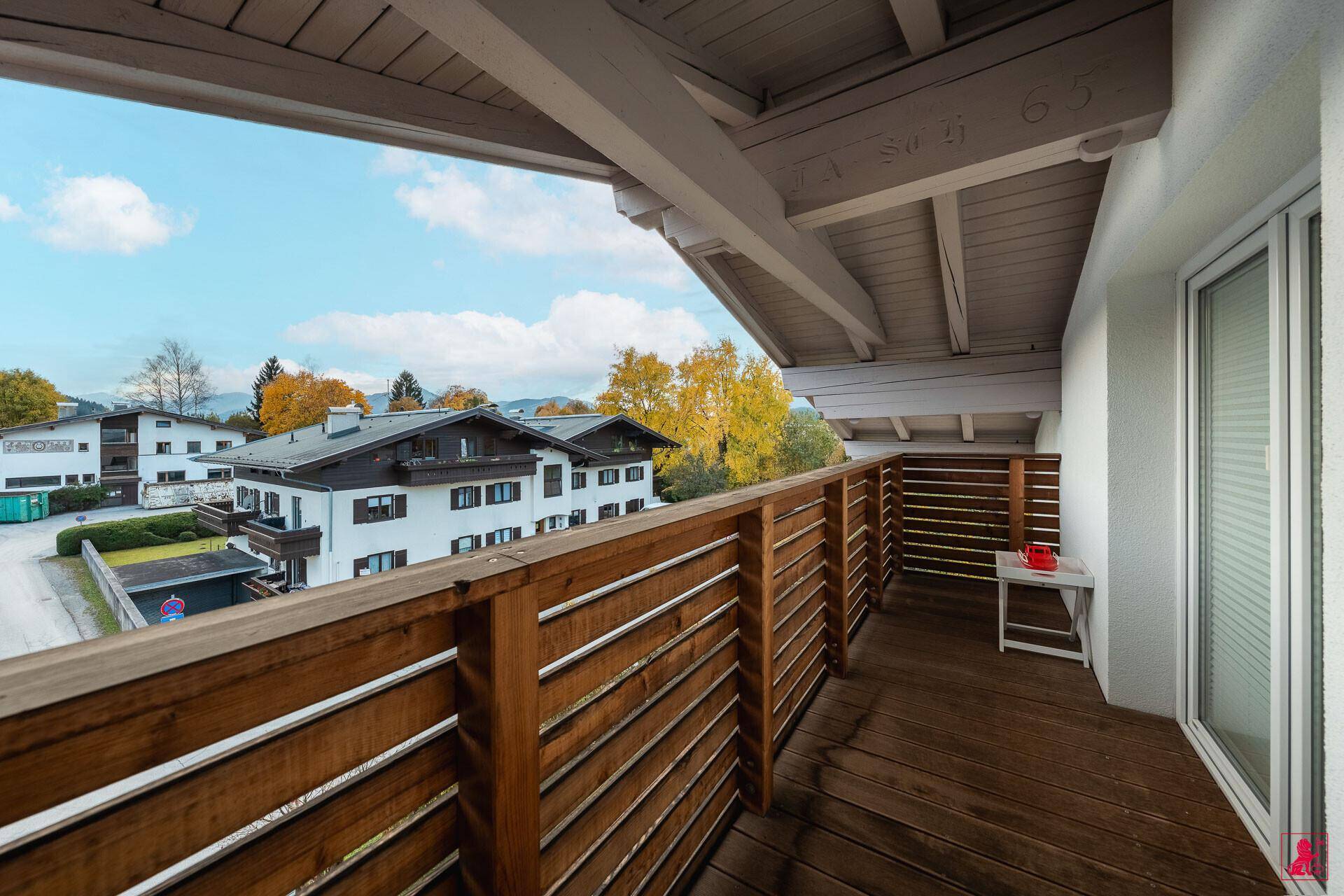 Überdachter Holzbalkon mit Blick auf die Nachbarschaft und die herbstliche Landschaft.