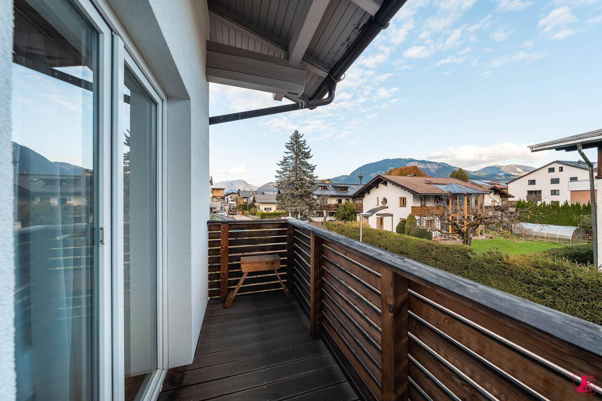 Geräumiger Balkon mit Holzboden und Geländer, bietet einen weiten Blick auf die umliegende Landschaft und Berge.