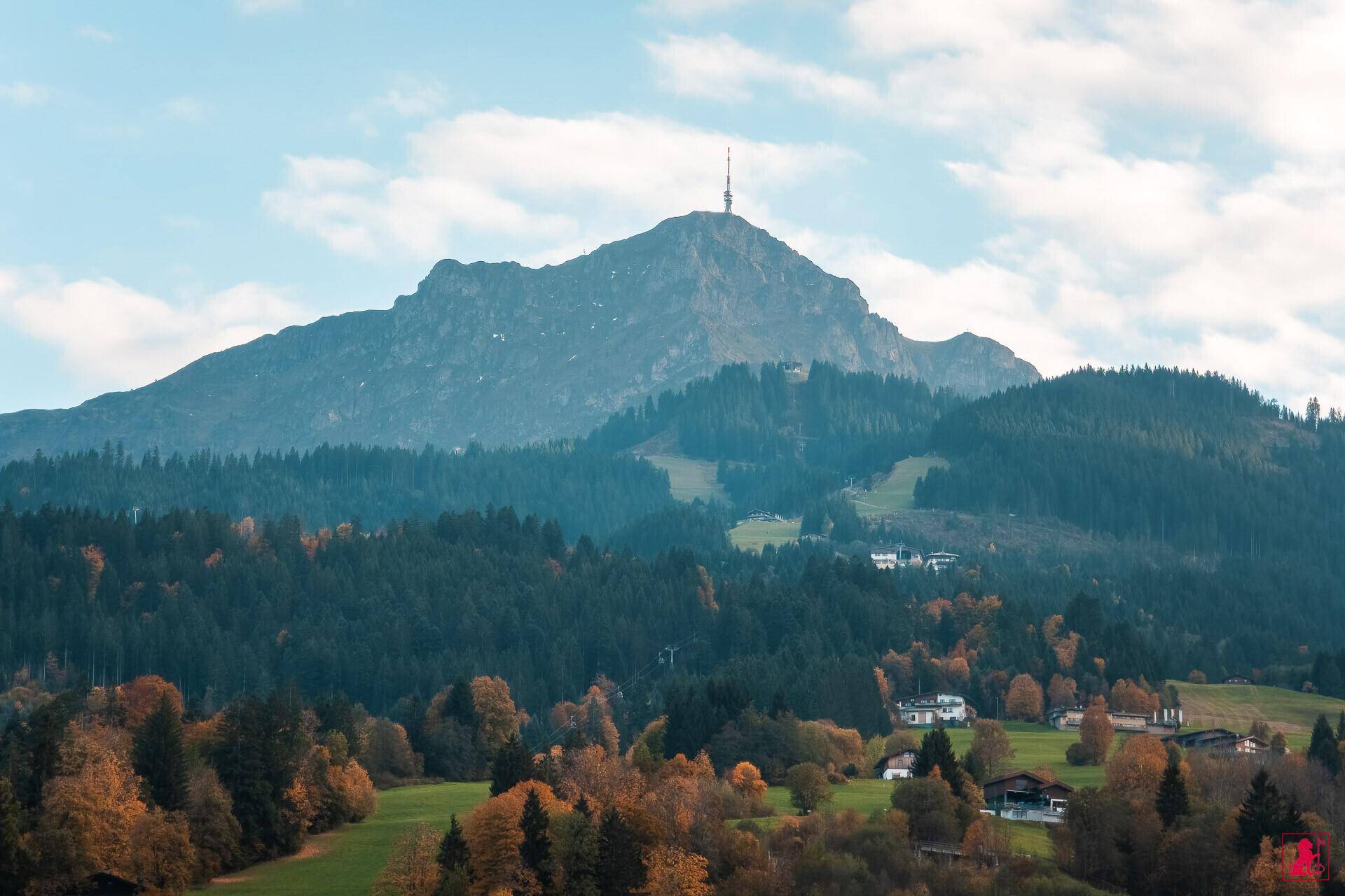 Malerische Berglandschaft mit herbstlichen Bäumen und vereinzelten Häusern.