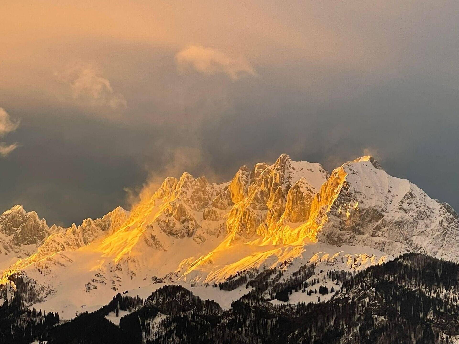 Spektakulärer Sonnenuntergang über schneebedeckten Berggipfeln, die im goldenen Licht erstrahlen.