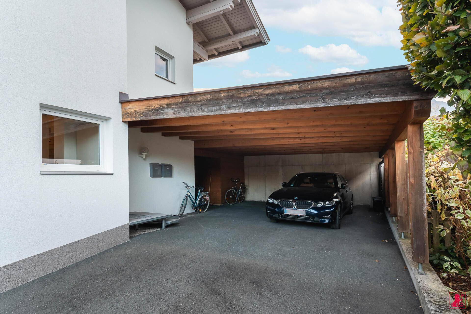 Überdachter Carport mit Holzbalken bietet geschützten Parkplatz für ein Auto und Fahrräder.