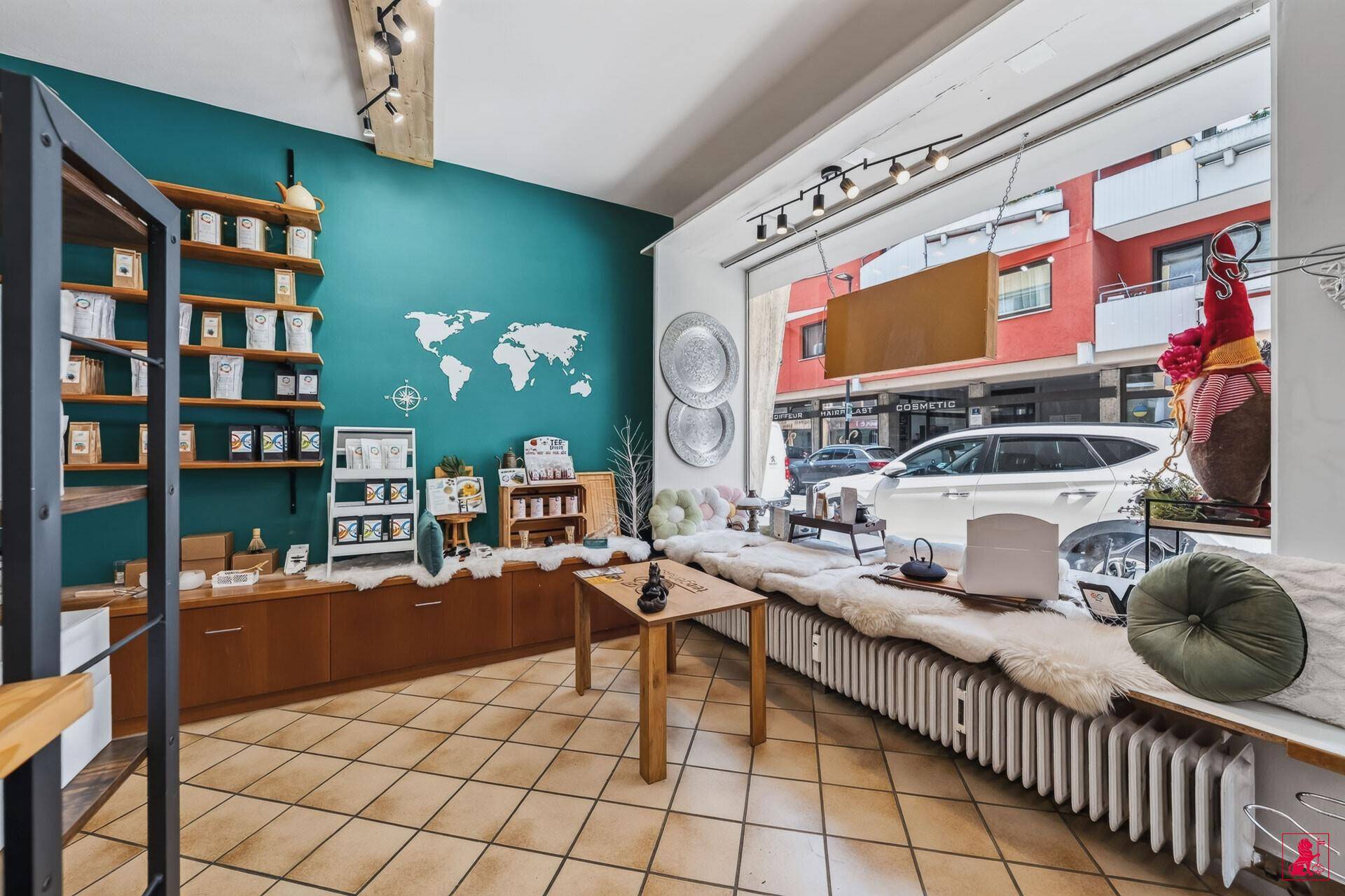 Gemütlicher Bereich am großen Schaufenster mit Sitzbank, Heizung und einer Weltkarte an der tealfarbenen Wand.