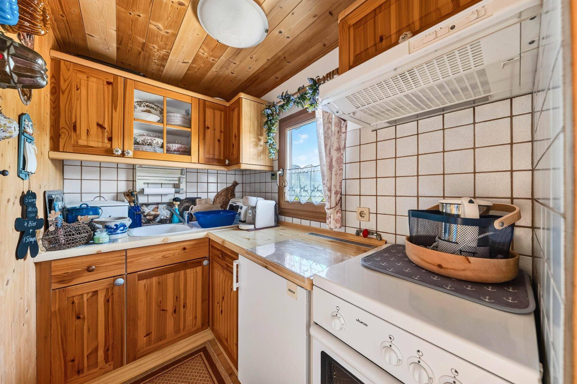 Kleine, funktionale Küche mit Holzschränken, Fliesenrückwand und Fenster im Landhausstil.