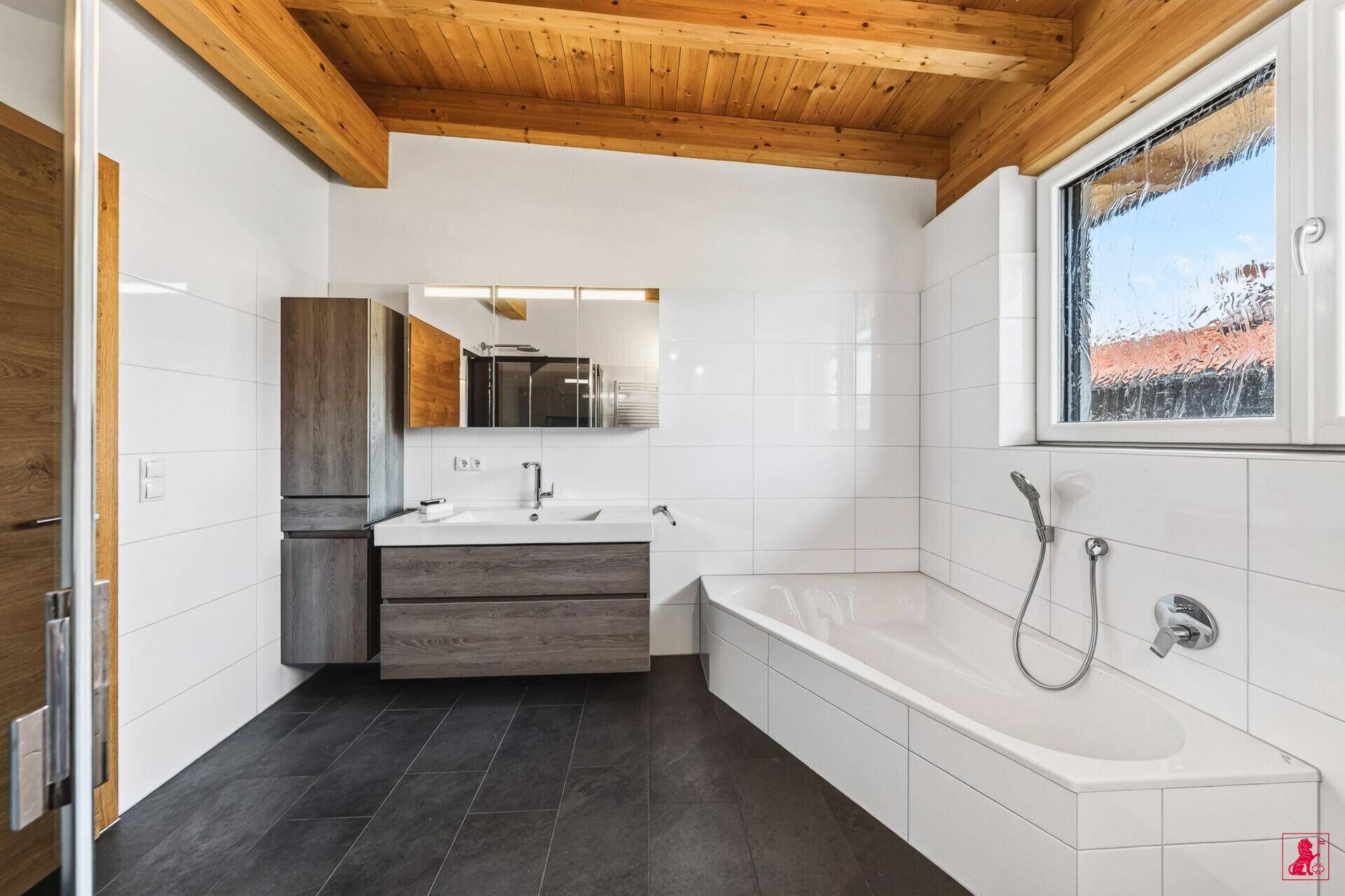Modernes Badezimmer mit Badewanne, Waschtisch und dunklen Bodenfliesen.