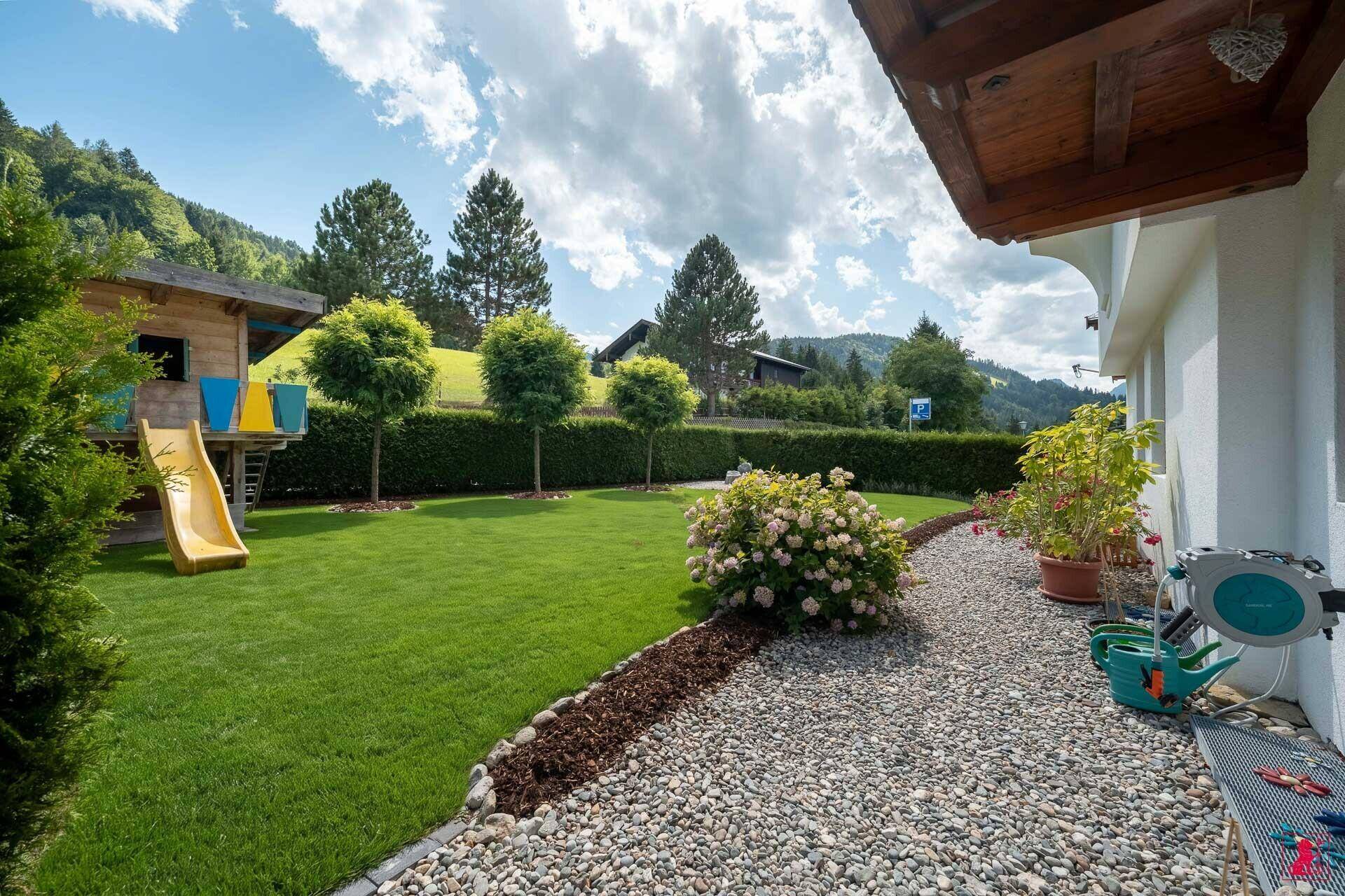 Gepflegter Gartenbereich mit Rasenfläche, Bäumen und einem Kinderspielgerät.
