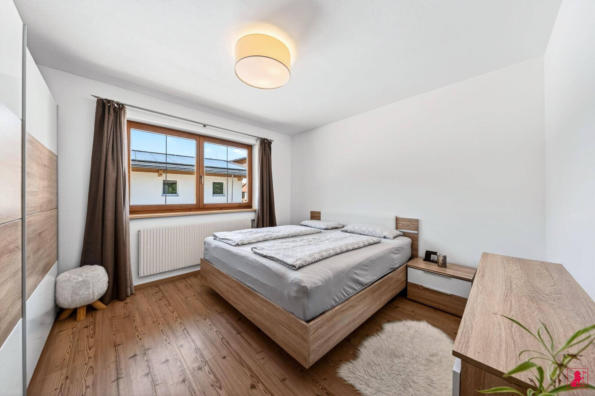 Helles Schlafzimmer mit Holzboden, Doppelbett und großem Fenster.