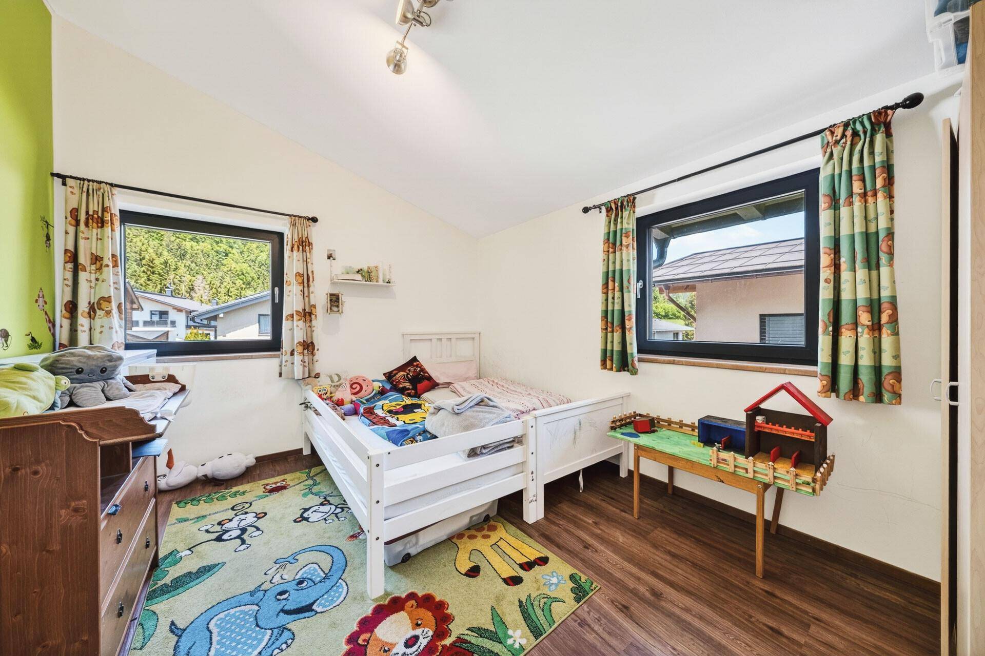 Kinderzimmer mit Einzelbett, Holzkommode und bunten Vorhängen, hell und freundlich.