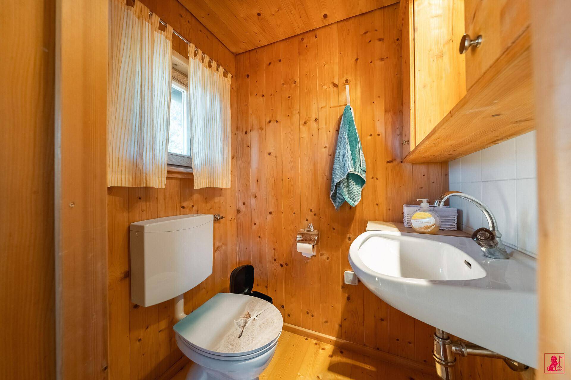Kleines WC mit Holzvertäfelung, Fenster und einfachem Waschbecken.