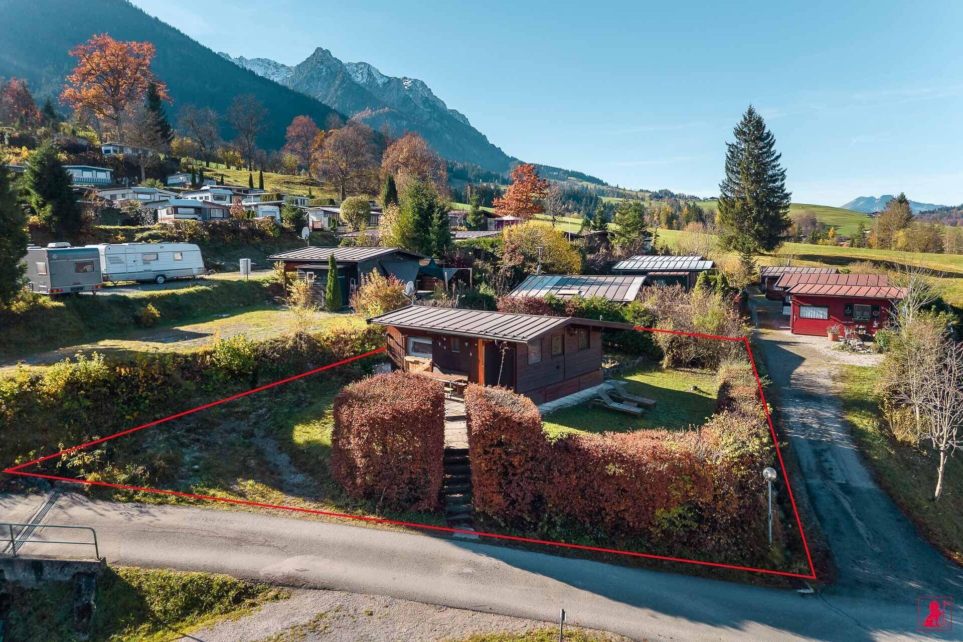 Luftaufnahme eines charmanten Holzhauses in alpiner Landschaft mit umliegenden Bergen und Grundstücksgrenzen.