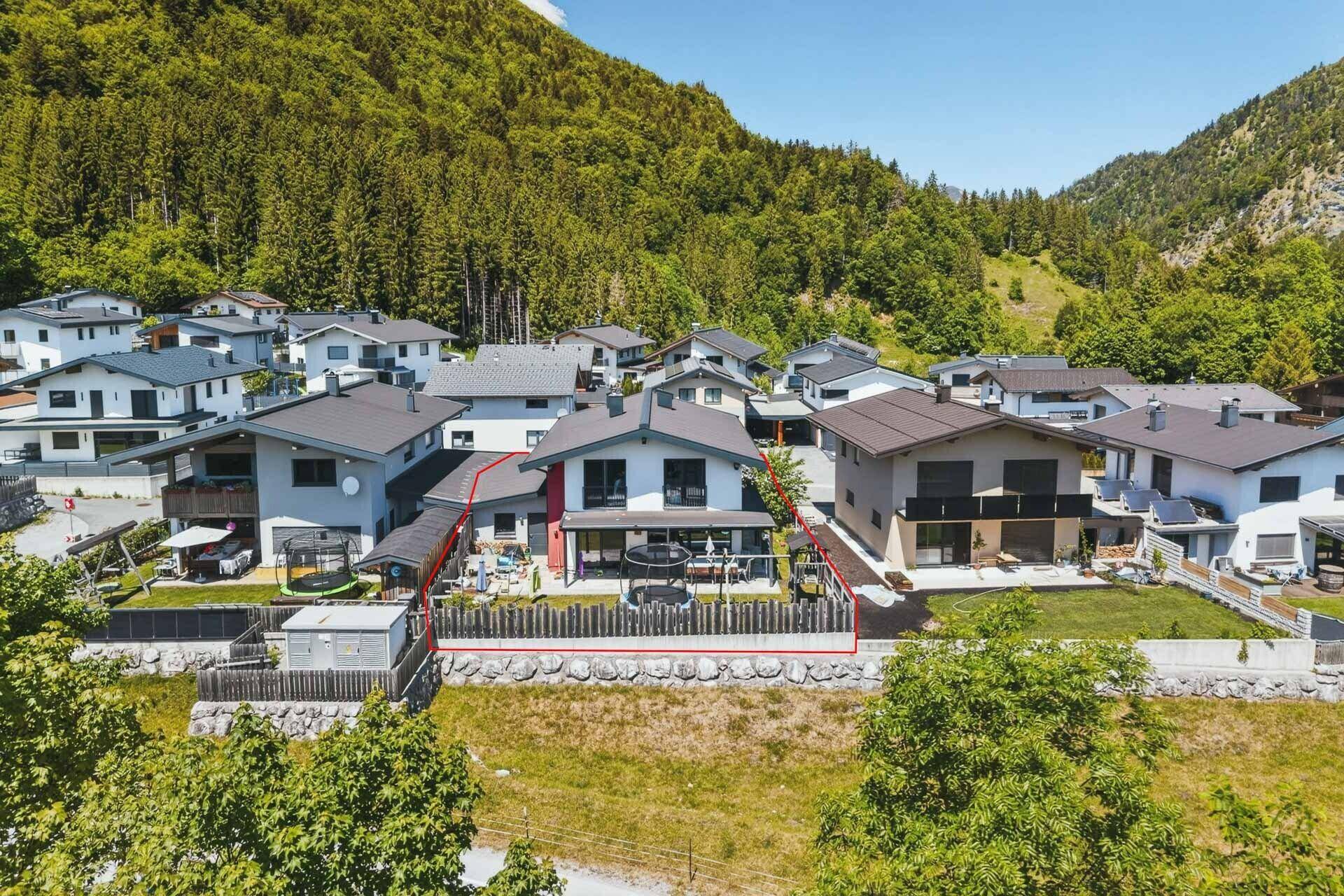Luftaufnahme eines modernen Einfamilienhauses mit Garten und Trampolin, umgeben von Natur.