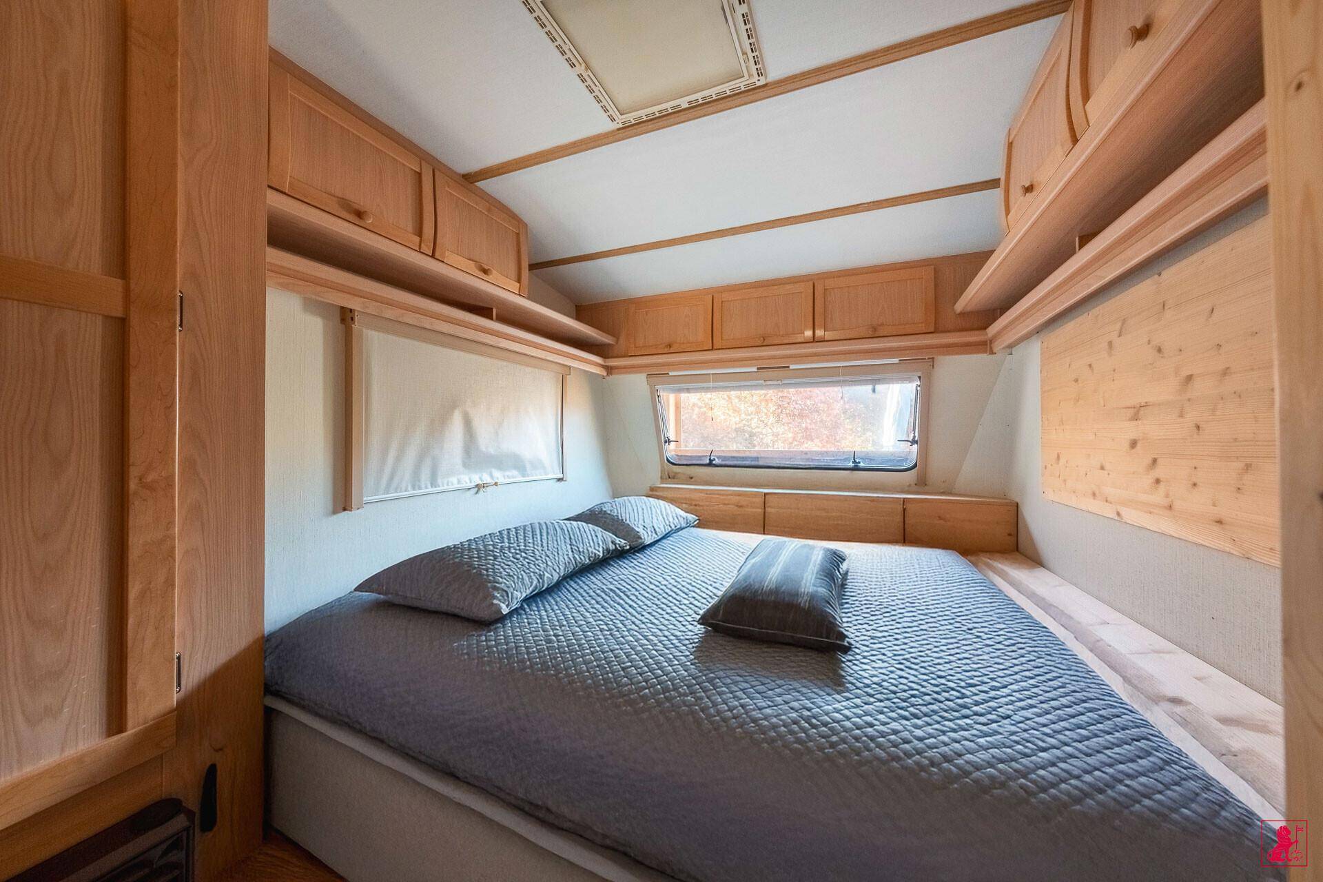 Kompaktes Schlafzimmer mit Doppelbett, Holzverkleidung und praktischen Stauschränken.