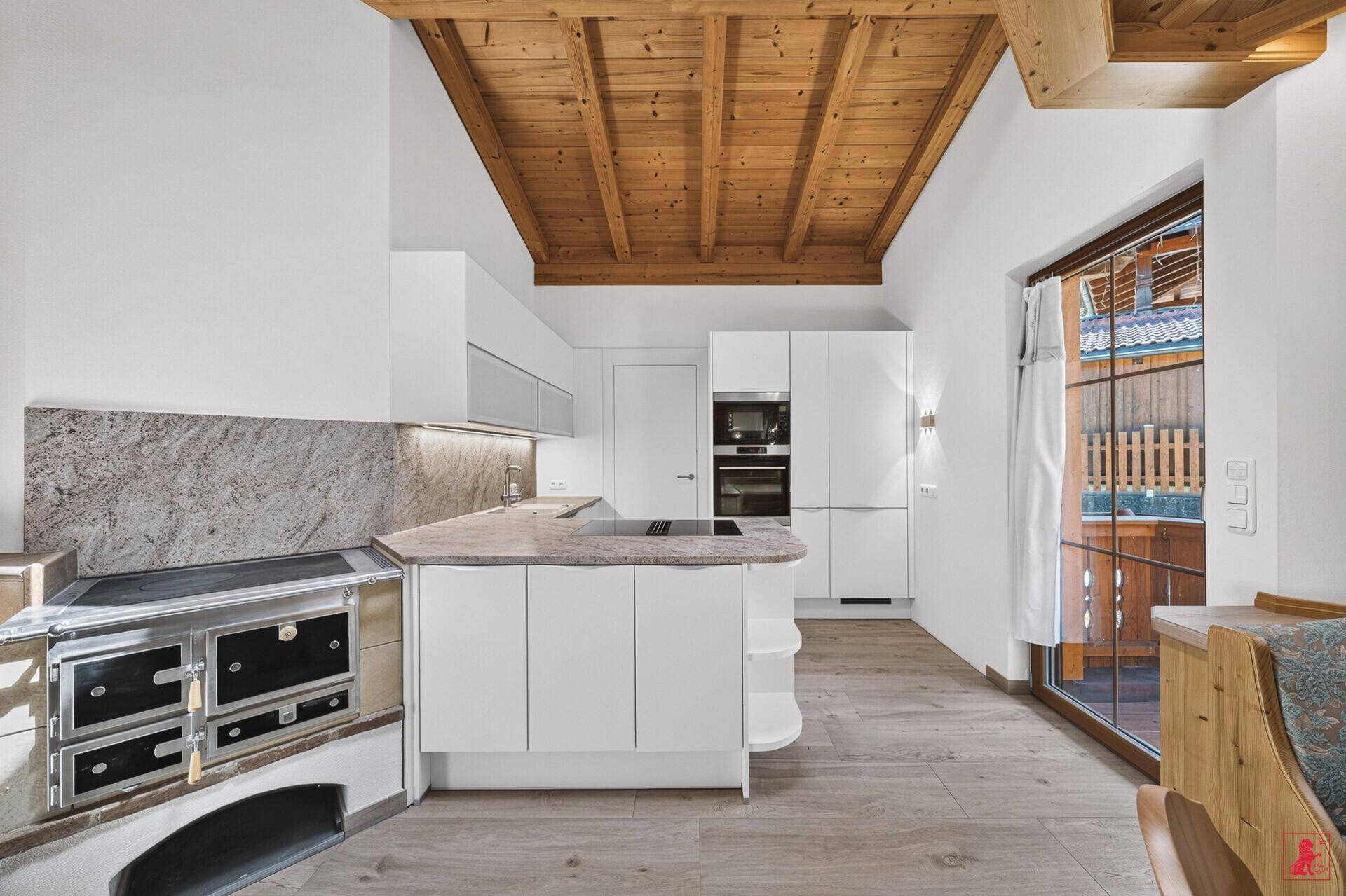 Moderne Küche mit Holzbalkendecke, integriertem Kachelofen und Zugang zu einem Balkon.