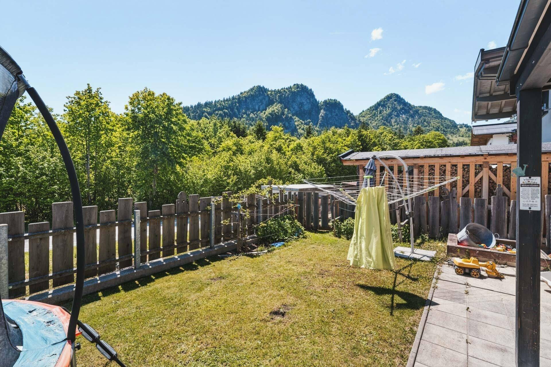 Gepflegter Garten mit Wäscheleine, Sandkasten und Blick auf die umliegende Berglandschaft.