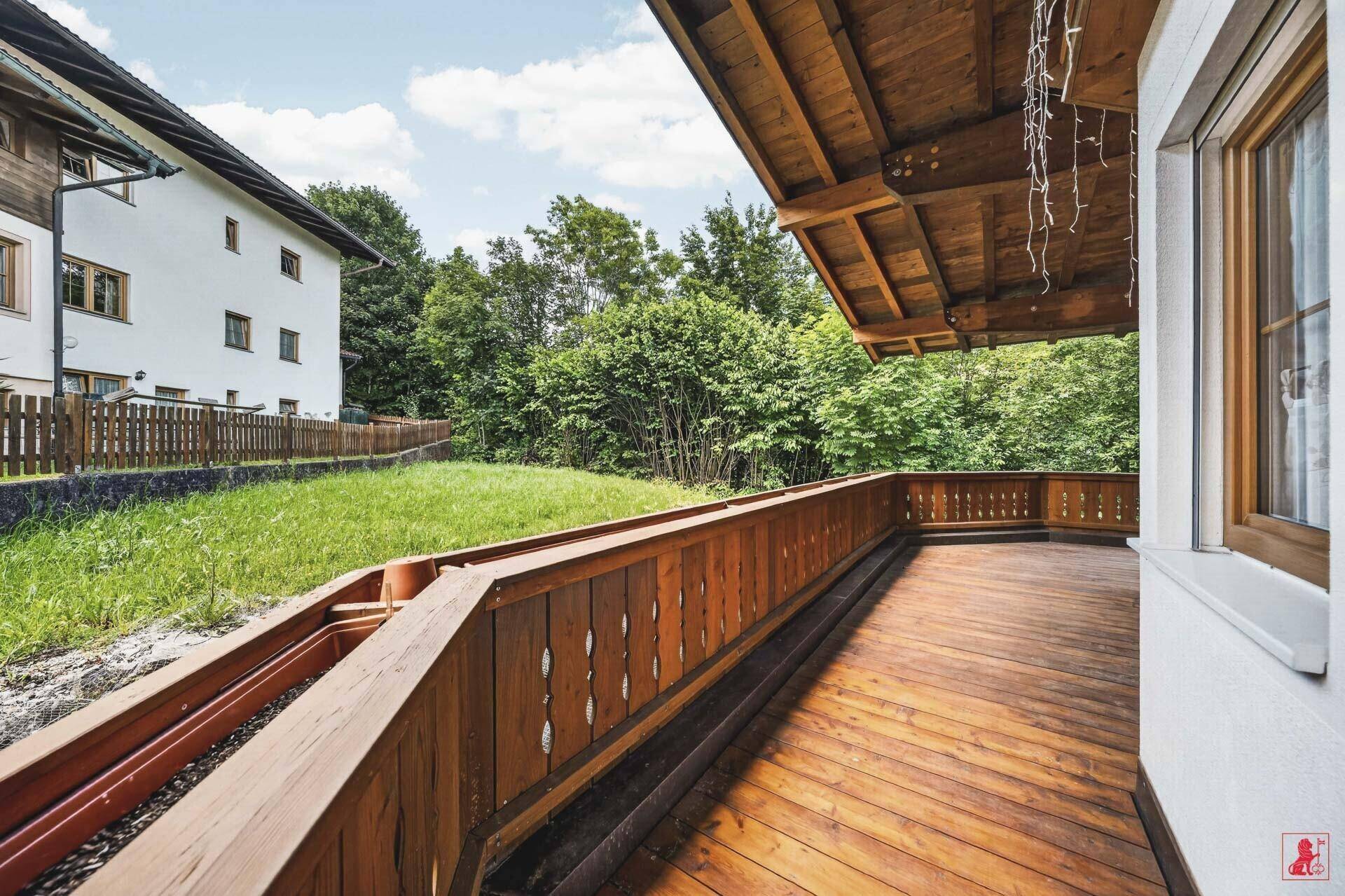 Geräumiger Holzbalkon mit Blick ins Grüne und angrenzender Rasenfläche.