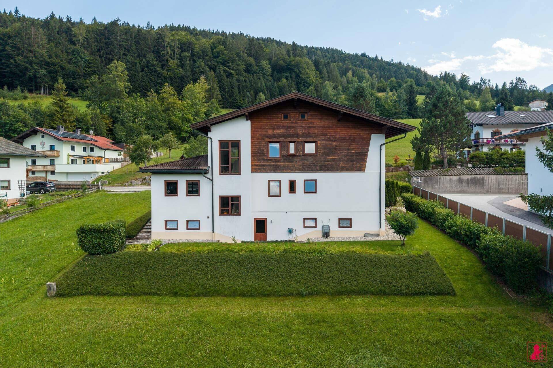 Rückansicht des Hauses mit grüner Wiese und bewaldeten Hügeln im Hintergrund.
