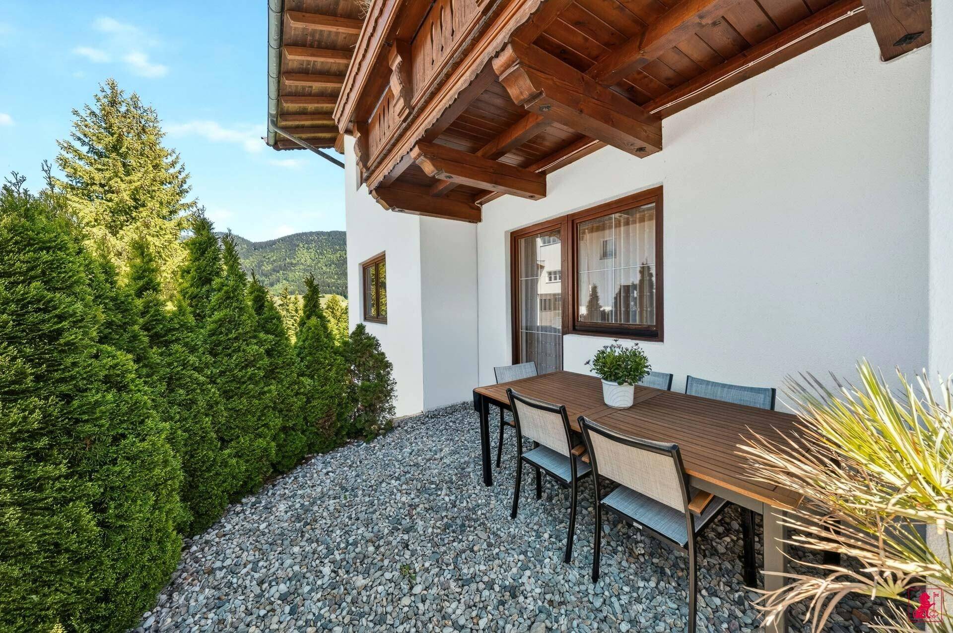 Gemütliche Terrasse mit Esstisch und Stühlen, umgeben von hohen Hecken.