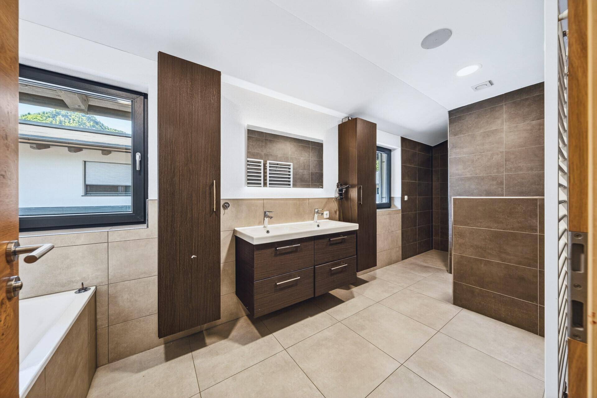 Geräumiges Badezimmer mit Doppelwaschbecken, Badewanne und modernen braunen Fliesen.