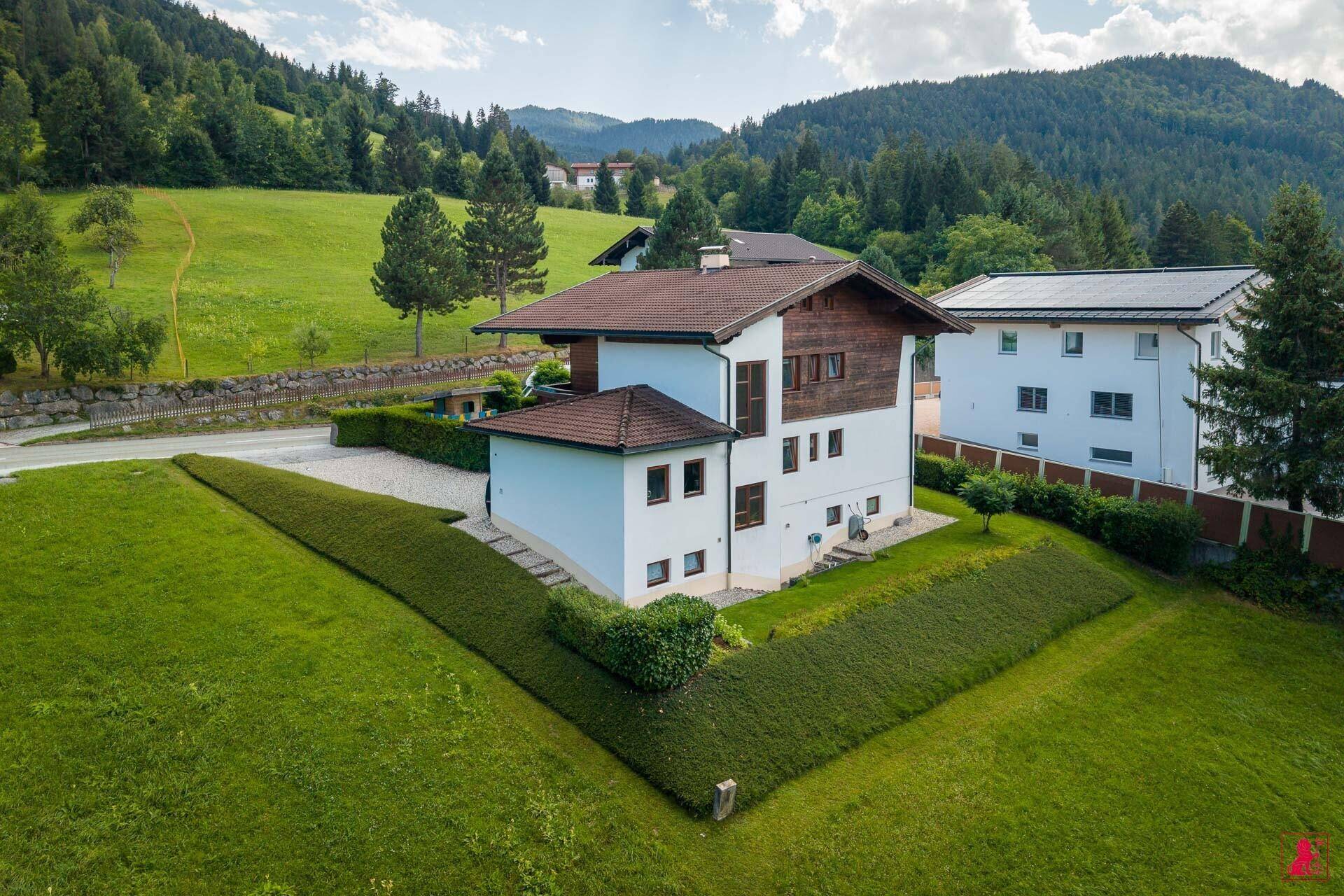 Luftaufnahme des Hauses in ländlicher Umgebung mit weitläufigen Grünflächen und Bergen.