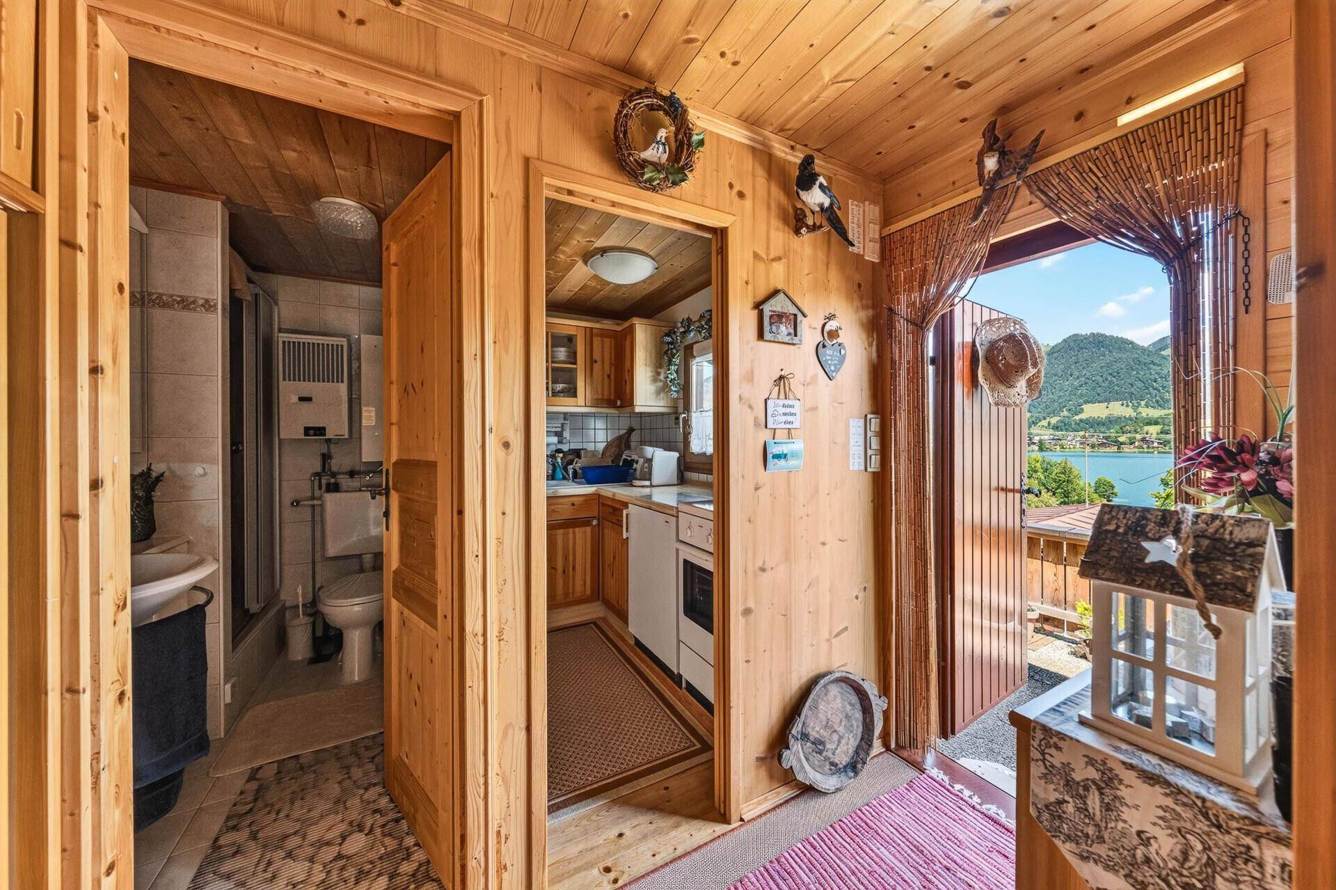 Gemütlicher Flur mit Holzwänden, Zugang zu Bad und Küche, und Seeblick durch die Tür.